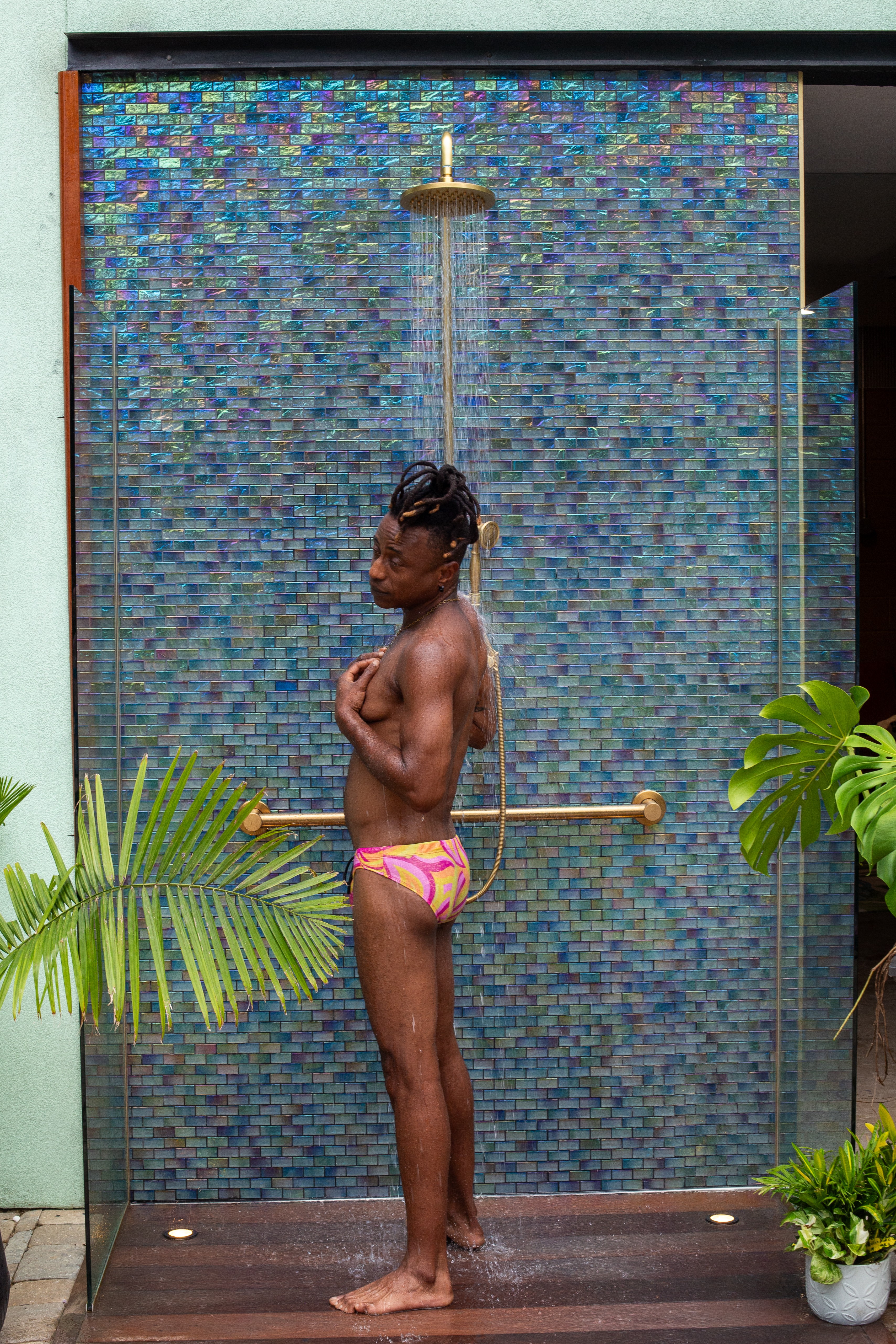 Child standing under a water feature with blue mosaic tiles, surrounded by green plants.