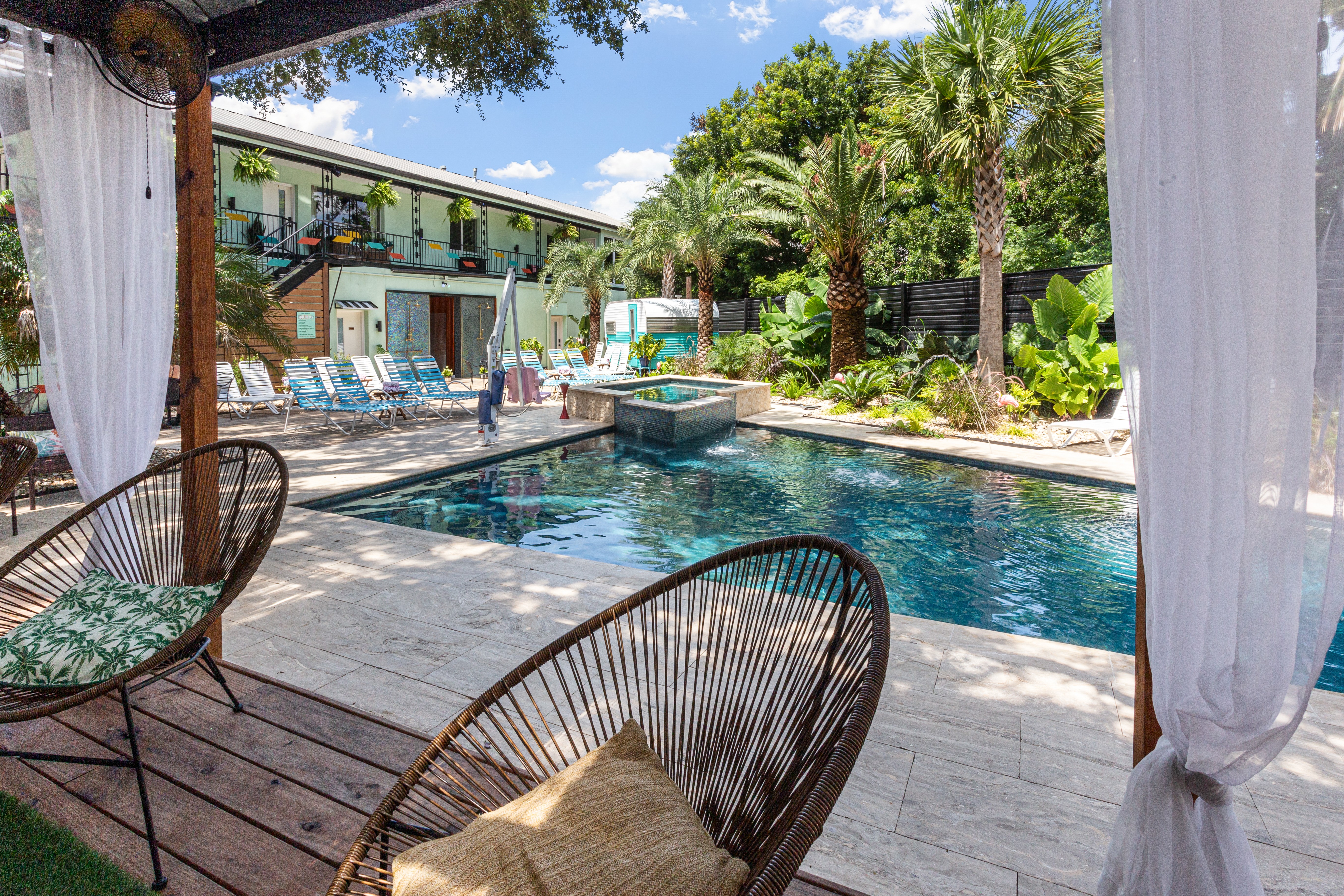 Poolside area with chairs, trees, and a swimming pool under a partly cloudy sky.