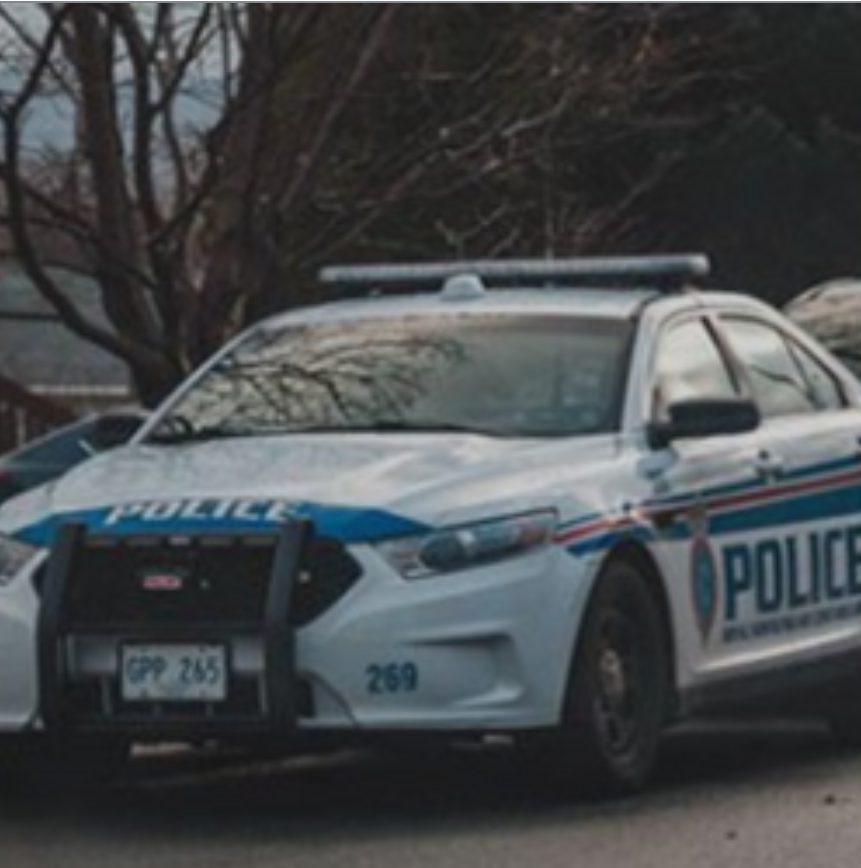 Police car parked outdoors with trees in background, front view, with police markings and equipment.