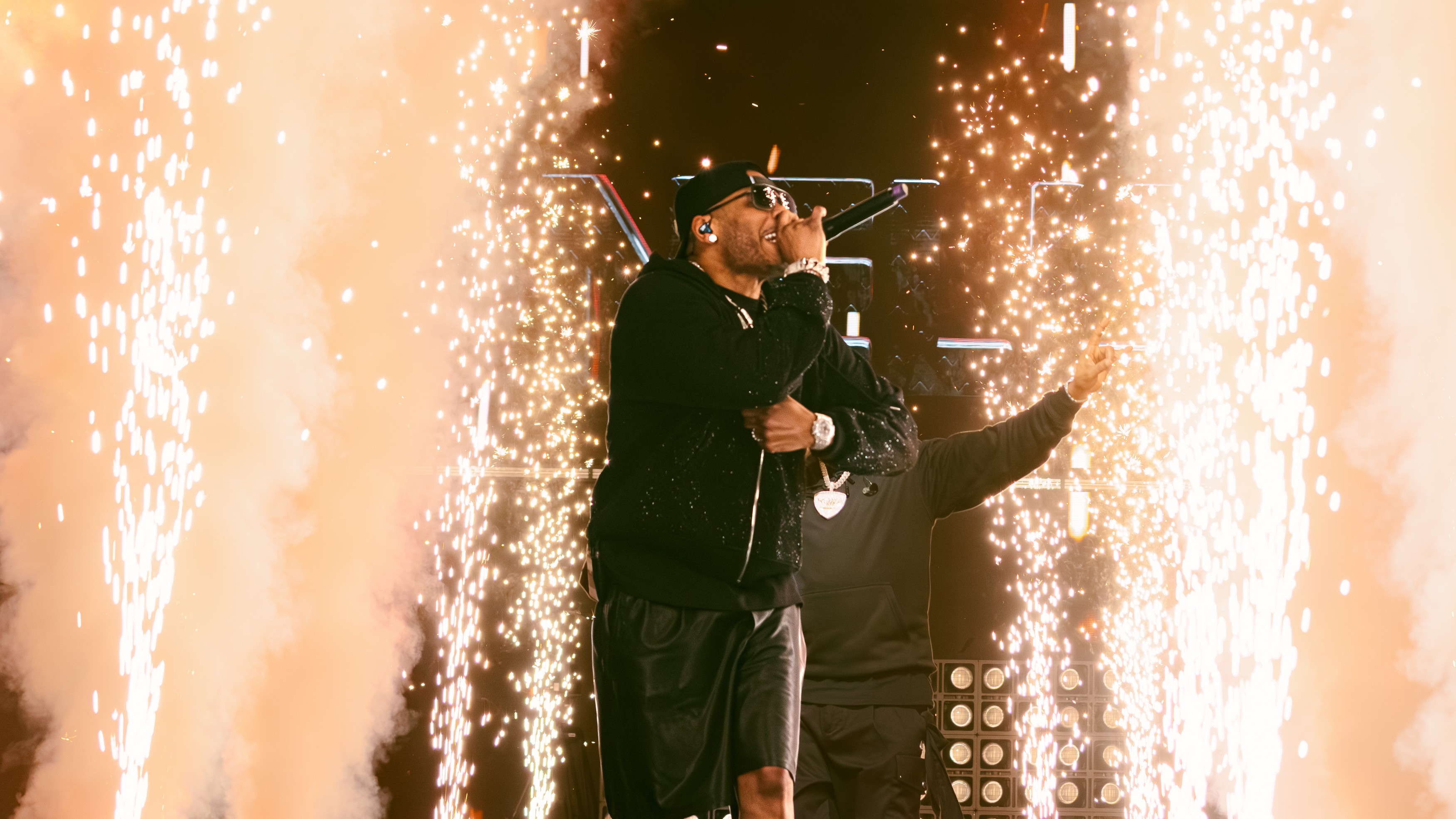 Performer singing into microphone with sparks and fireworks around on stage.