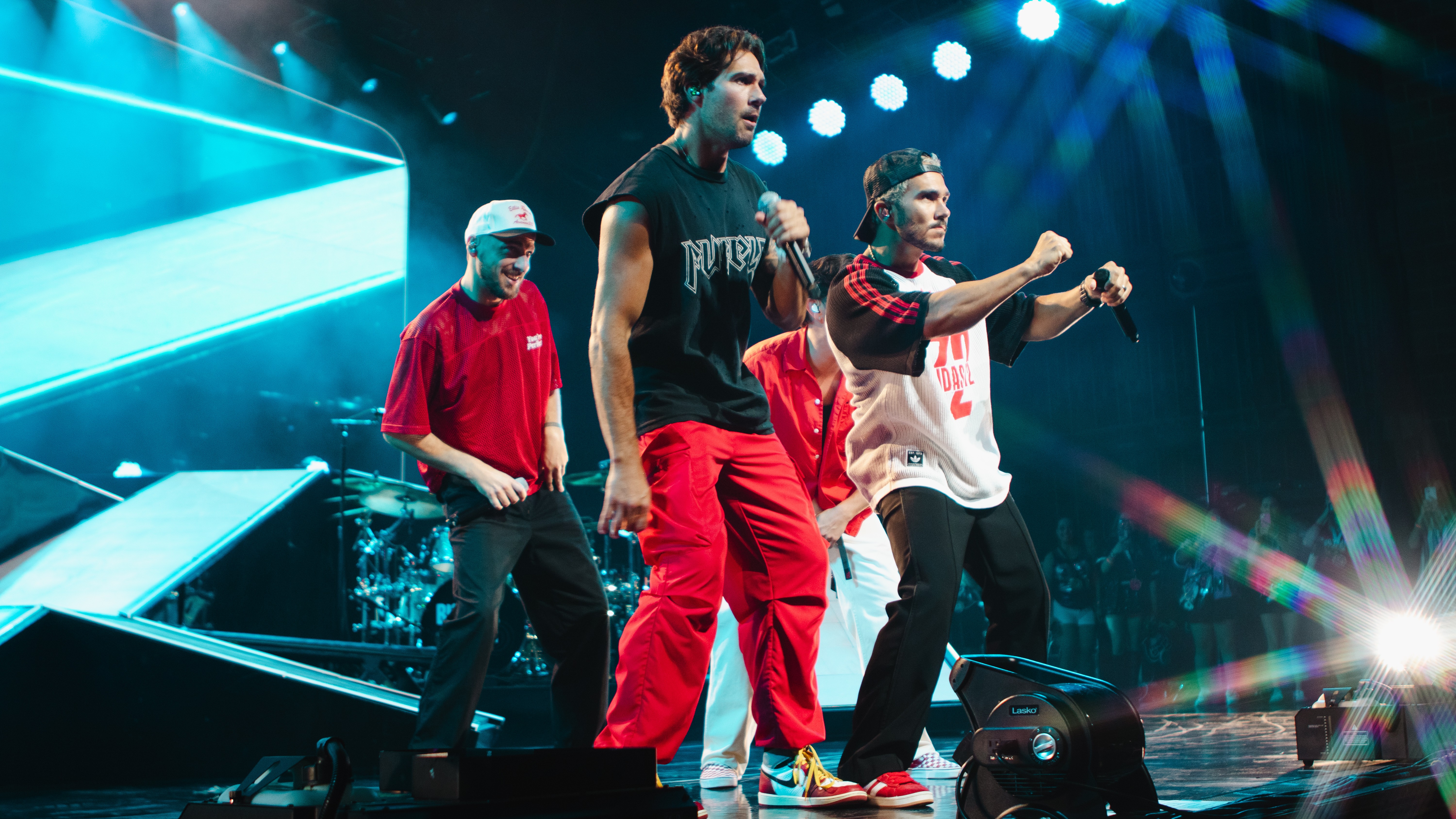 Four performers on stage with colorful lighting and a large screen in the background.
