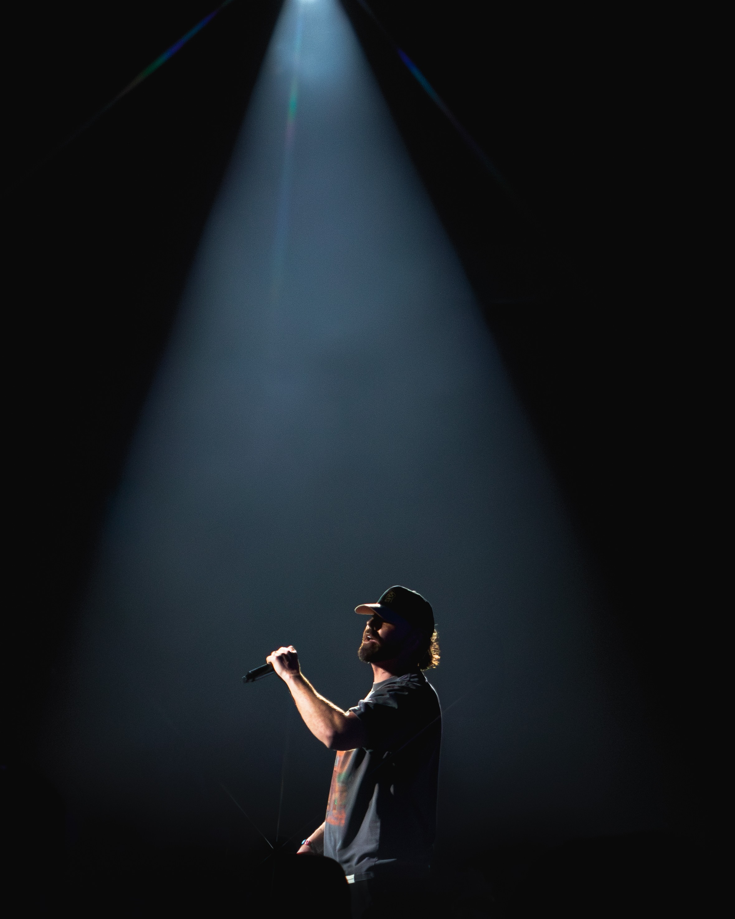 Person holding a microphone on stage under a spotlight in a dark environment.