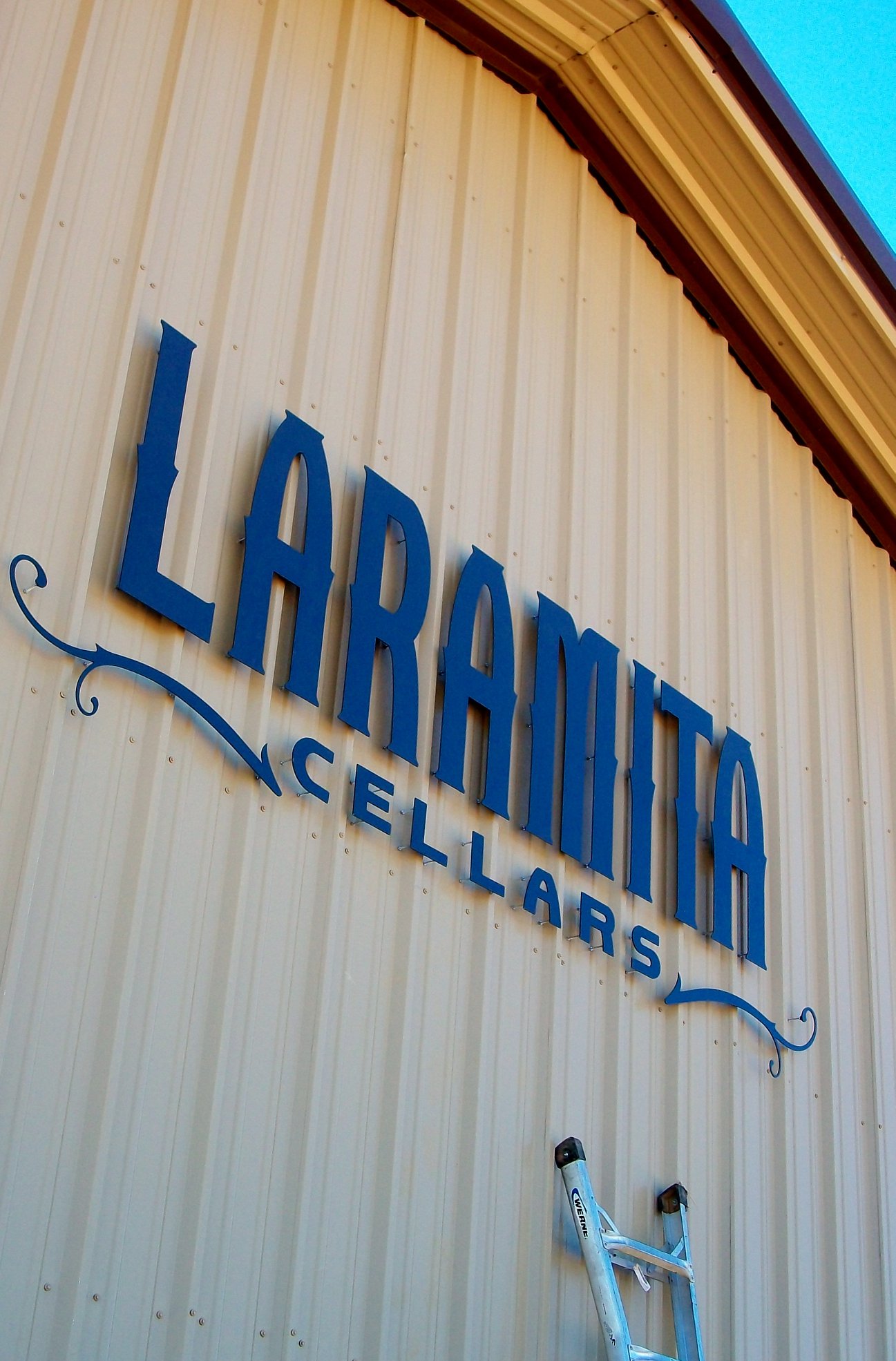 Sign reads LARAMA CELLARS on a beige vertical siding building exterior.