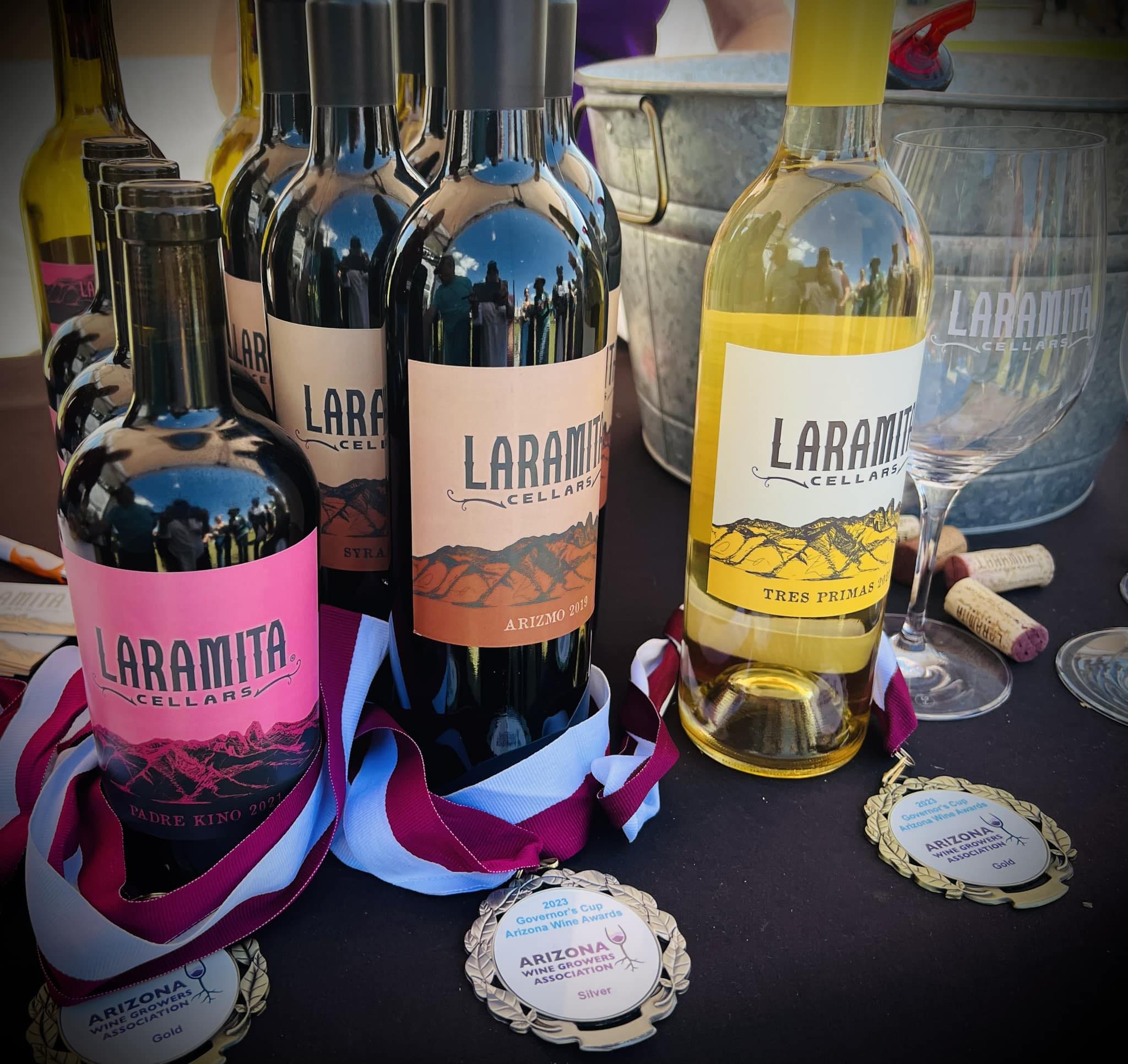 Bottles of wine with colorful labels and medals on a table, some with ribbons, in front of a large bowl.