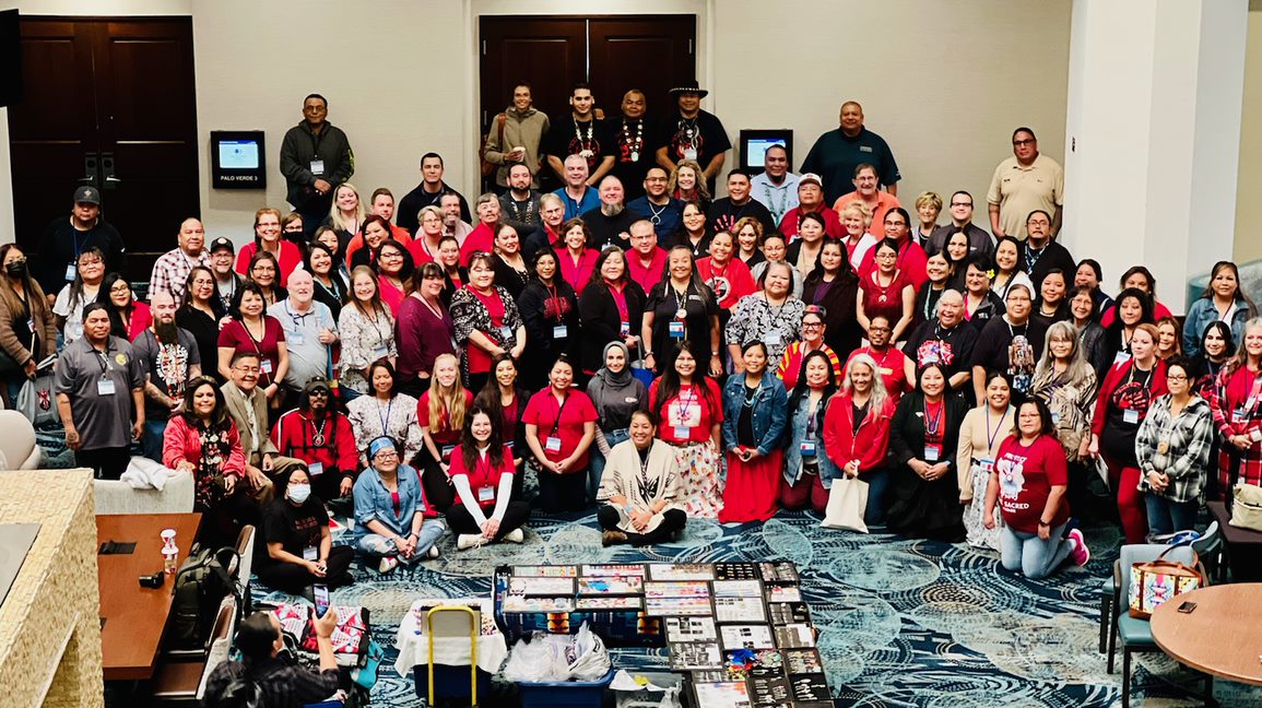 Large group of people gathered in a spacious room, some wearing red shirts, posing for a group photo.