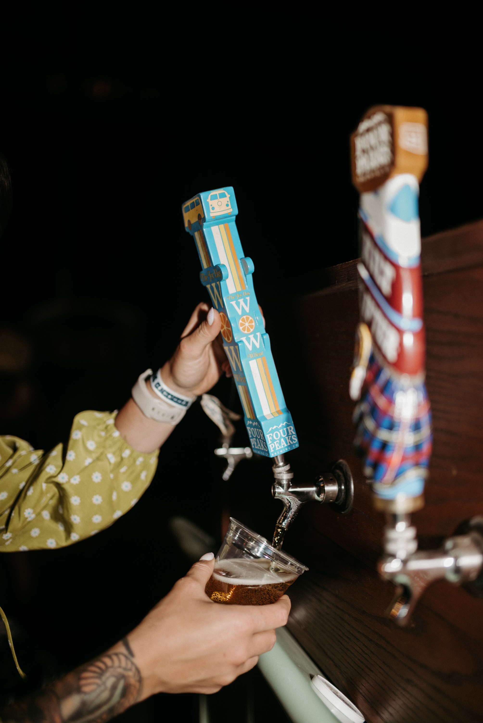 Person pours beer from tap into glass, with colorful tap handles in background.