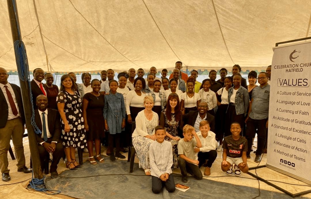 Group of people gathered inside a tent, posing for a photo with a banner on the right side.