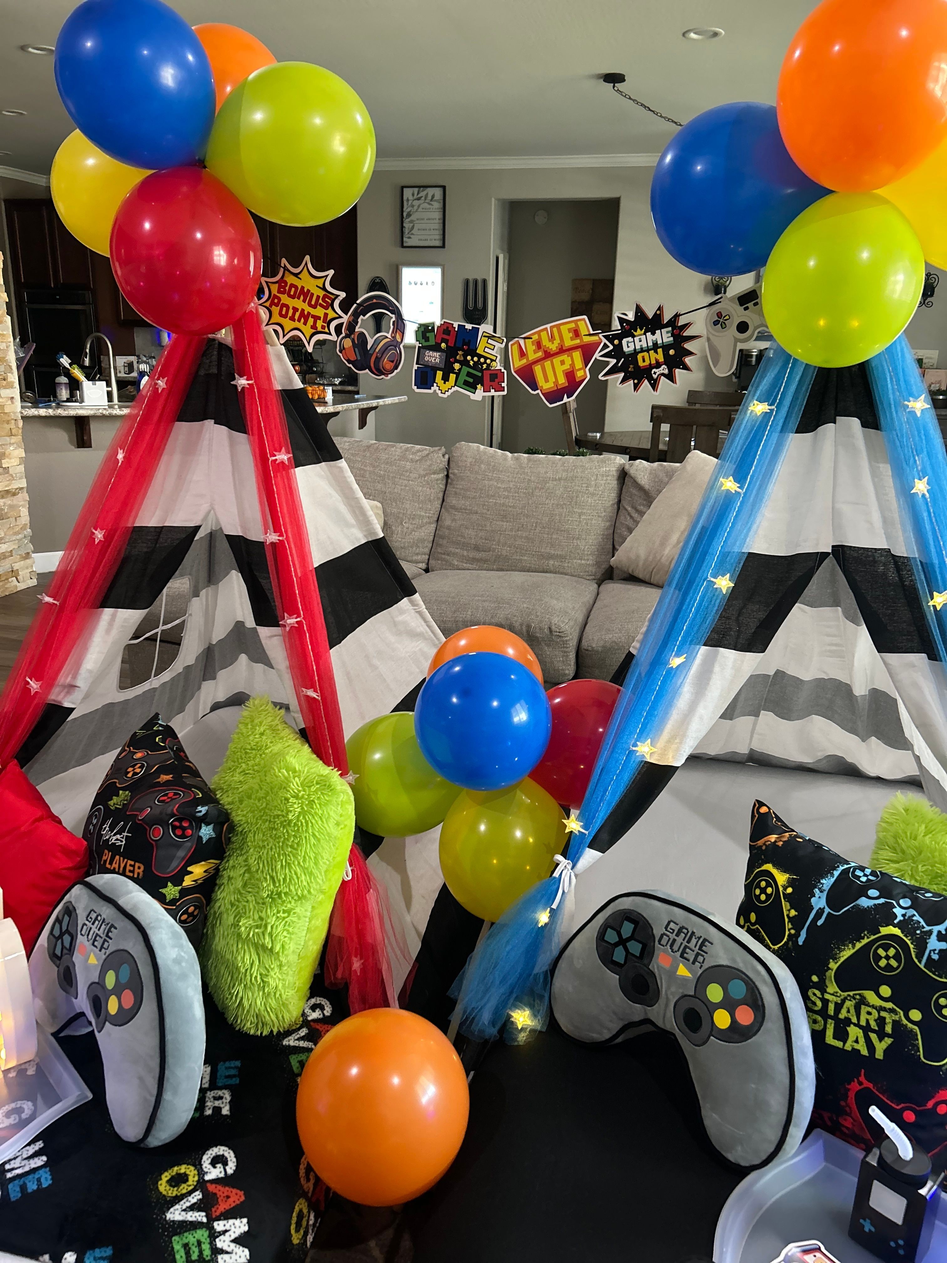 Indoor space with two small tents decorated with balloons, gaming controllers, and star-themed banners.