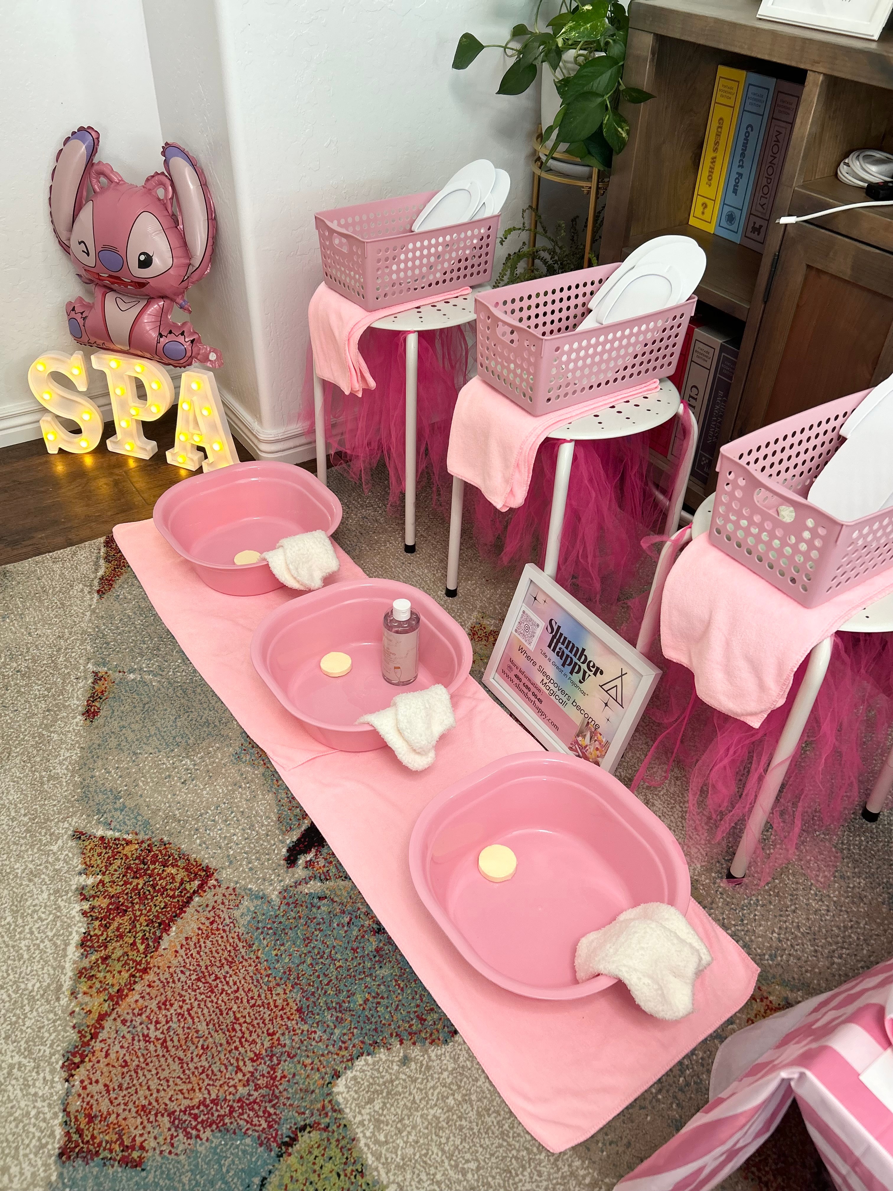 Spa setup with pink basins, towels, and chairs, decorated with a pink balloon, in a cozy room corner.