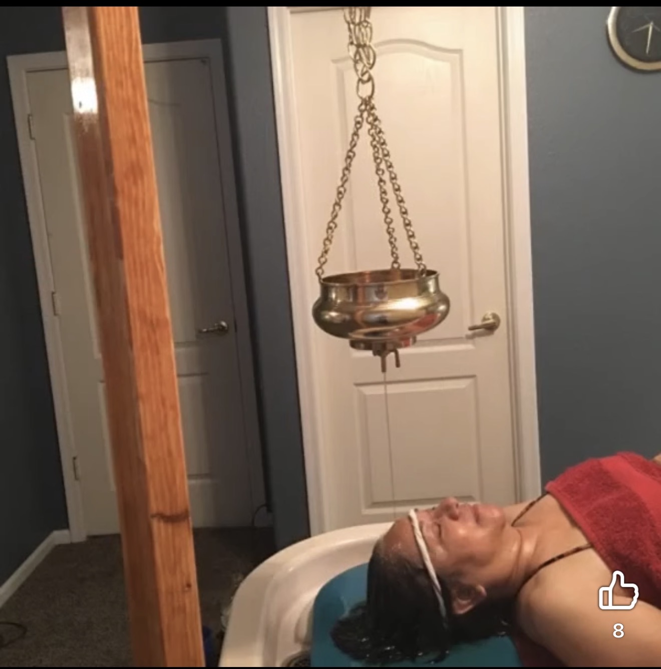 Person lying on a white chair with a red towel on head, in a room with blue walls and white door.