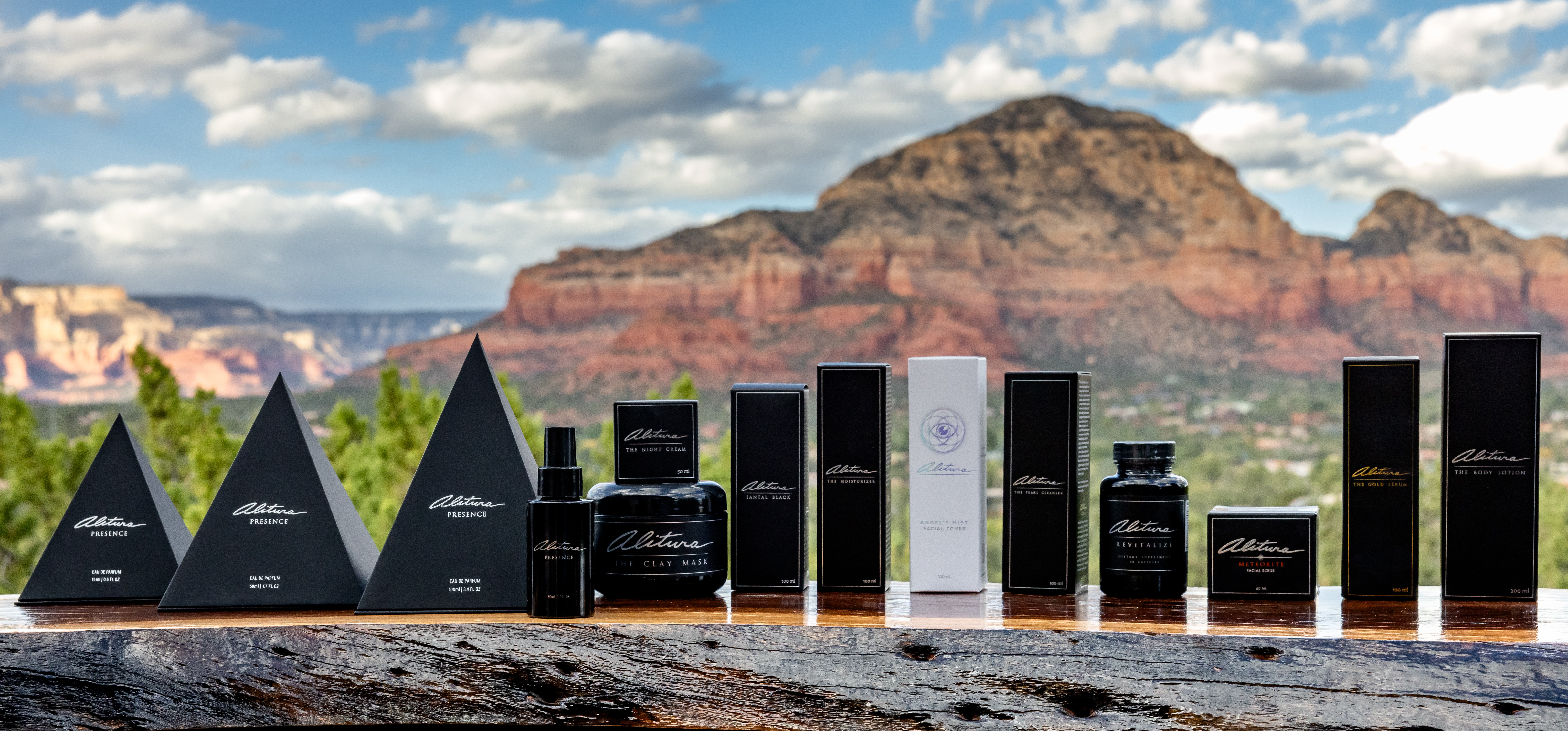 Collection of black and white skincare or cosmetic products on a surface with a mountain and cloudy sky background.