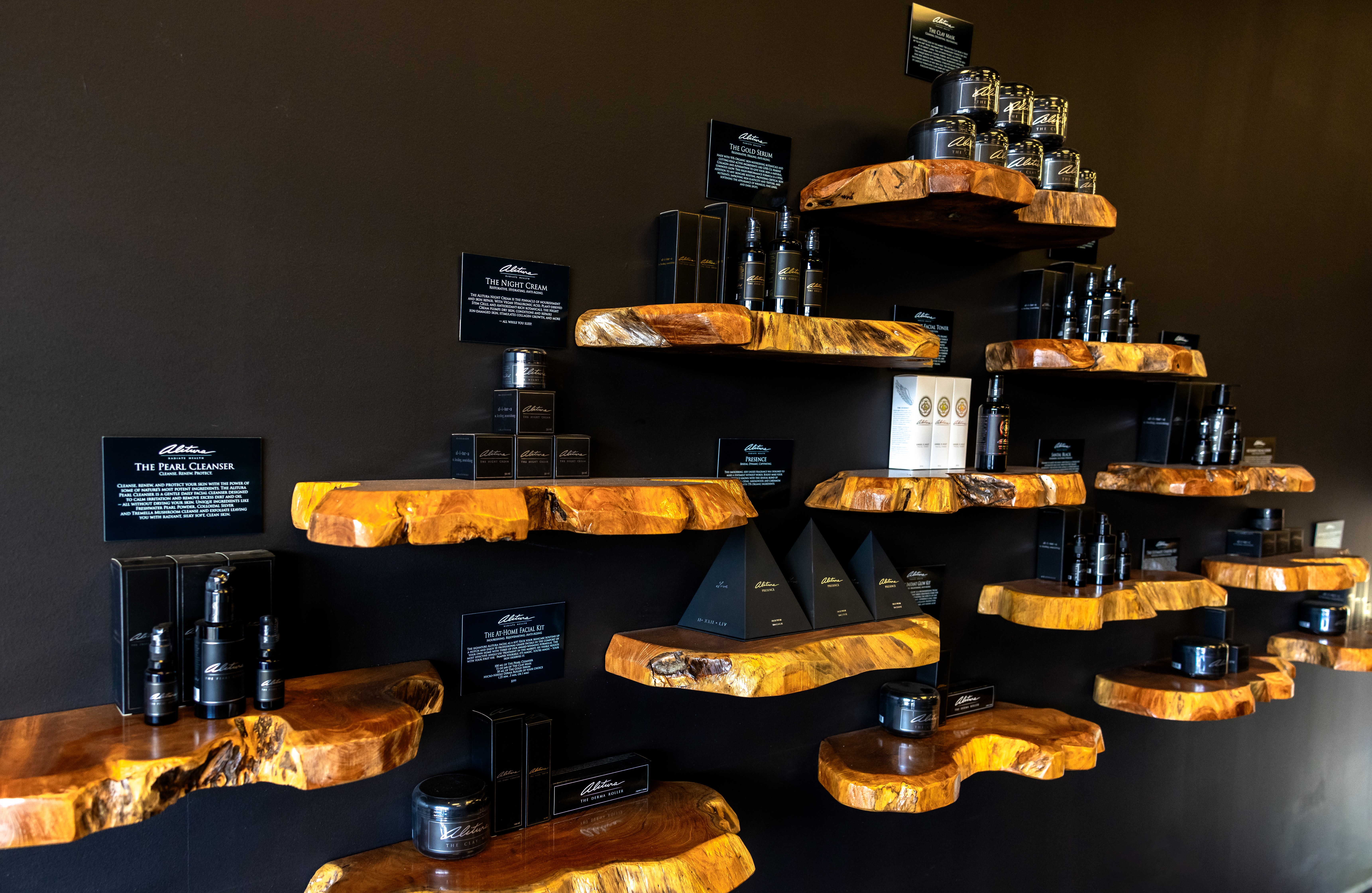 Display of black bottles and glasses on wooden shelves against a dark wall.