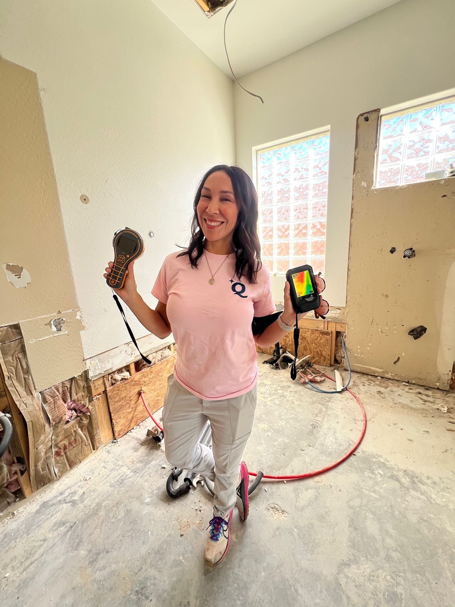 Woman smiling, holding a power drill and a multimeter in a room under renovation.