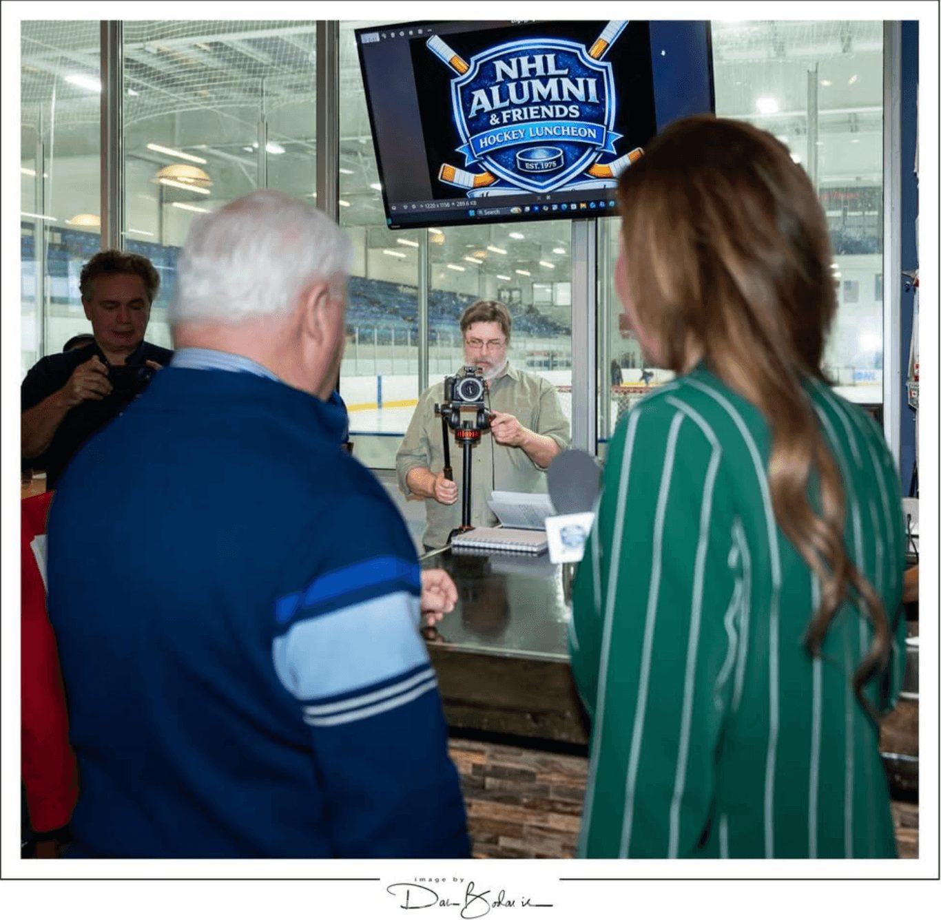 People at a reception desk with a screen displaying 'NHL Alumni & Friends' in the background.