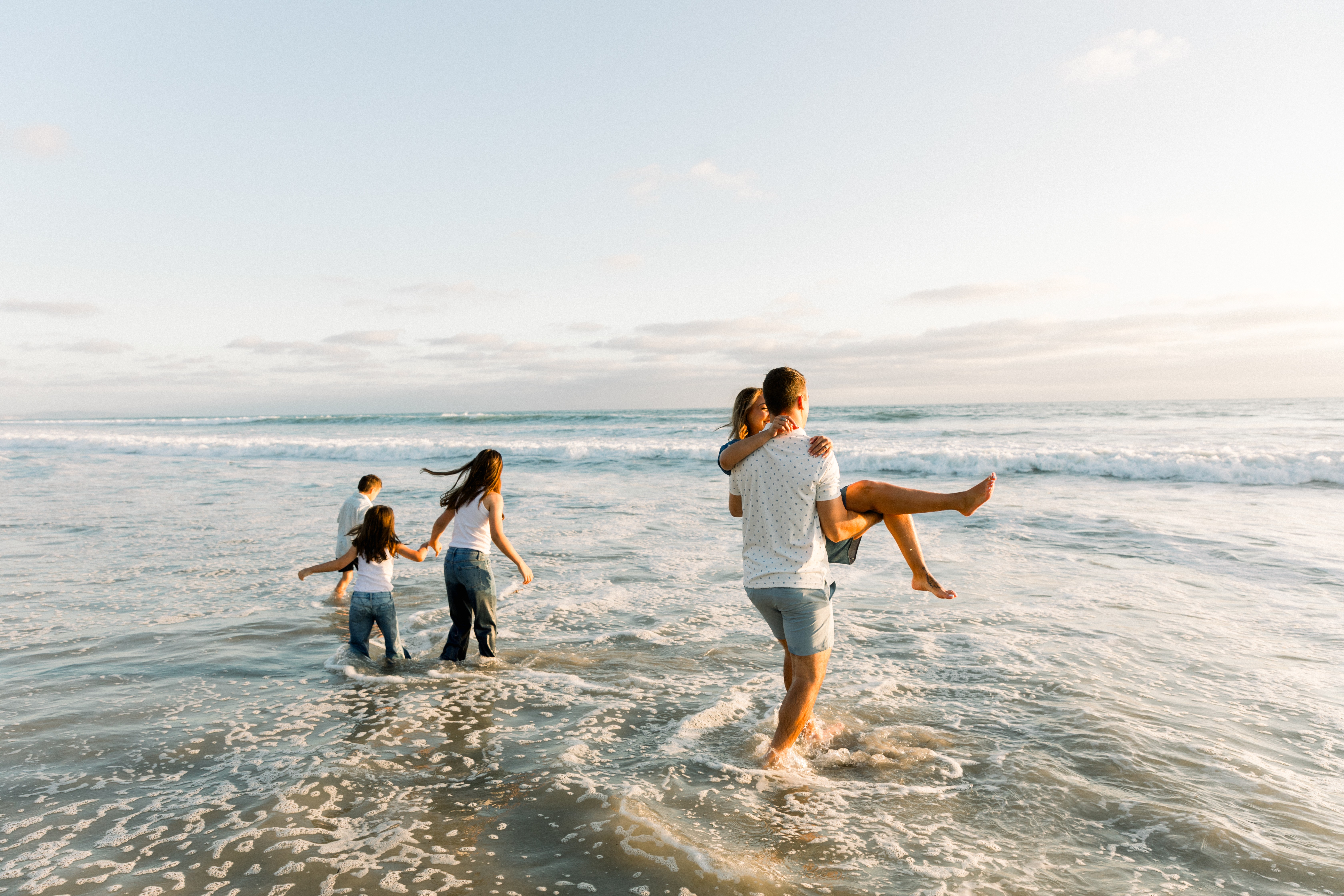 Four people, including children, enjoy the beach near the water's edge during sunset or sunrise.