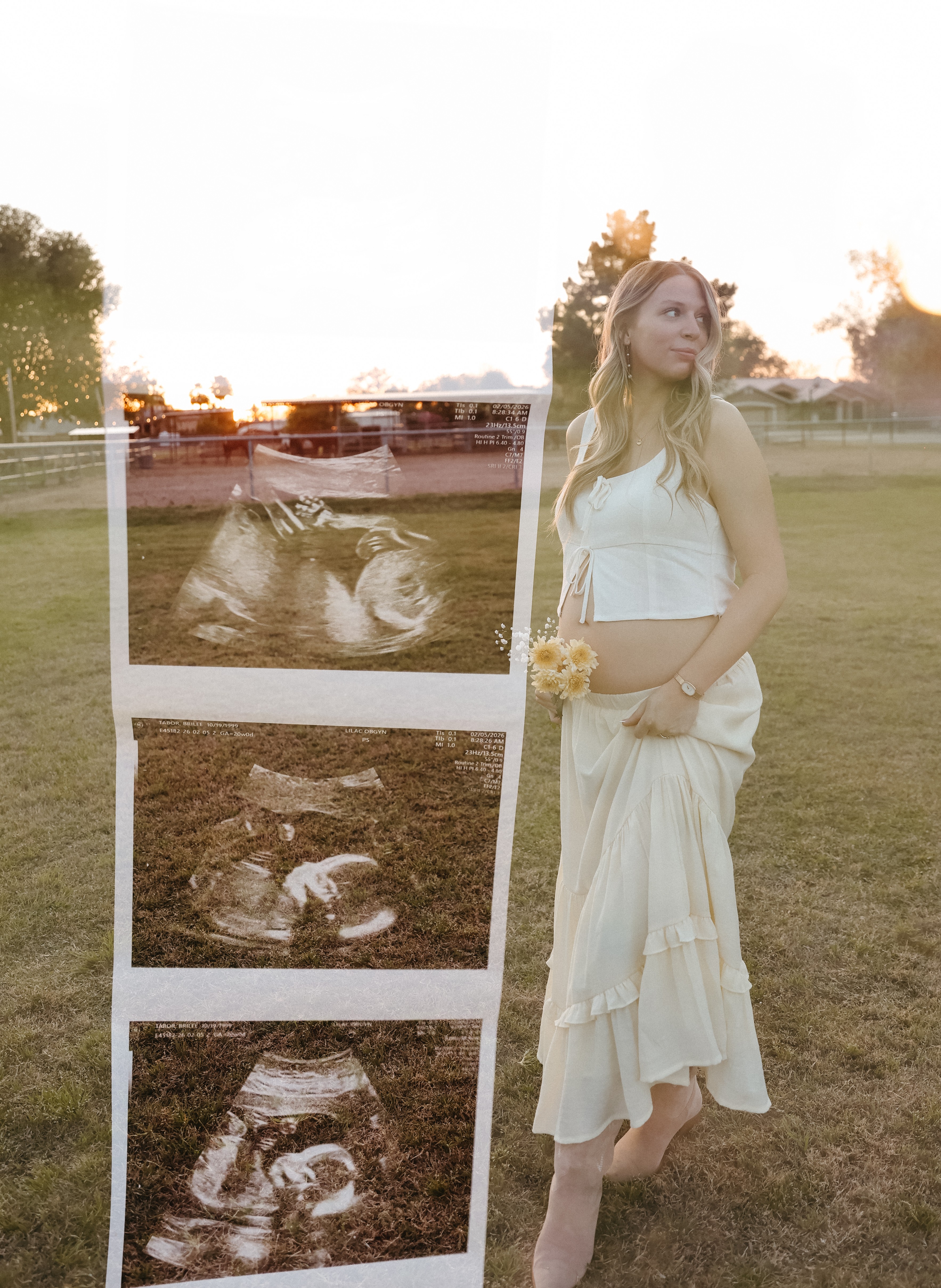 A pregnant woman in a white dress stands outdoors near a display of ultrasound images, with trees and a field in the background.