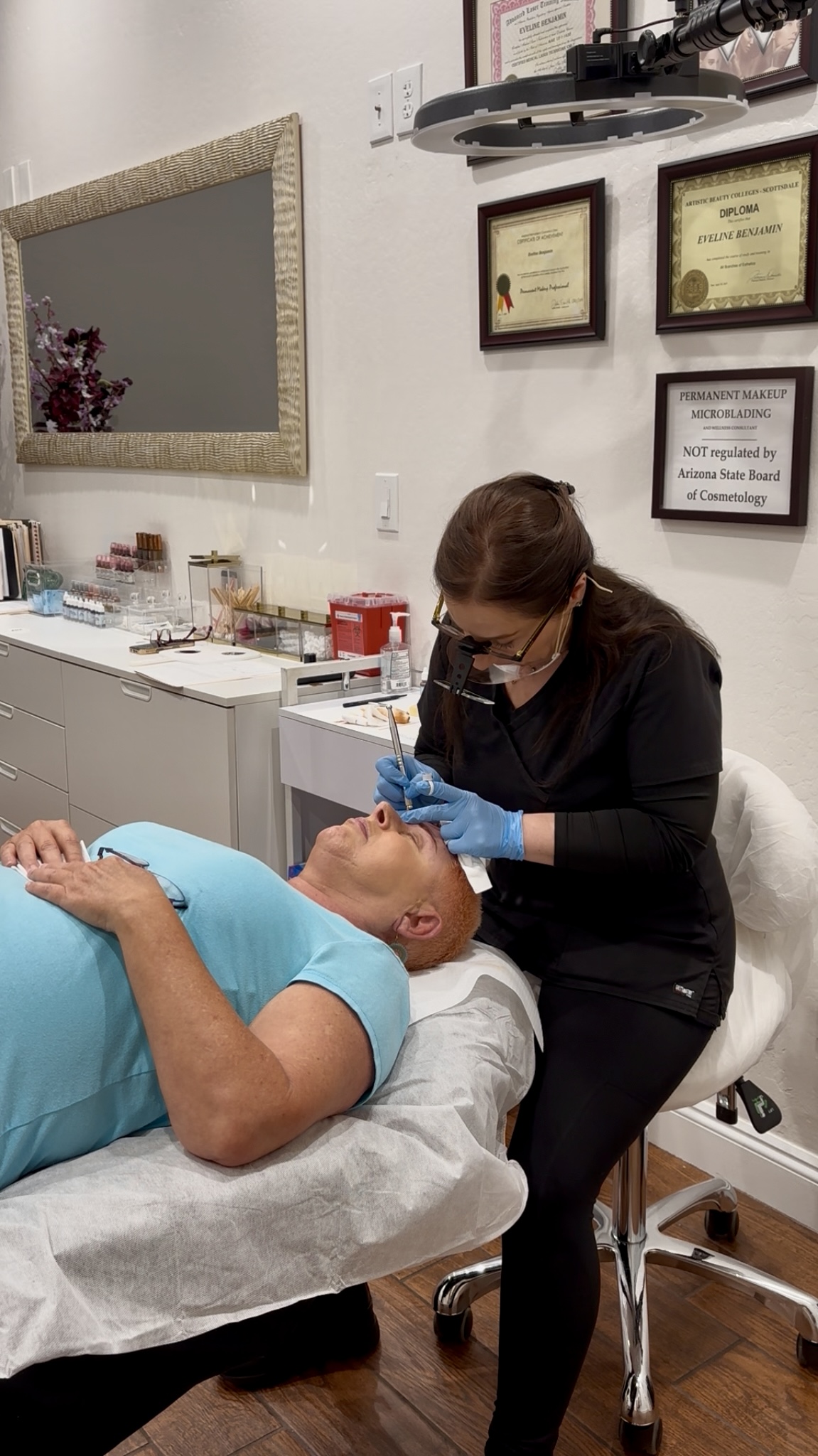 A healthcare professional examines a patient lying on a bed in a clinical setting, with framed certificates on the wall.