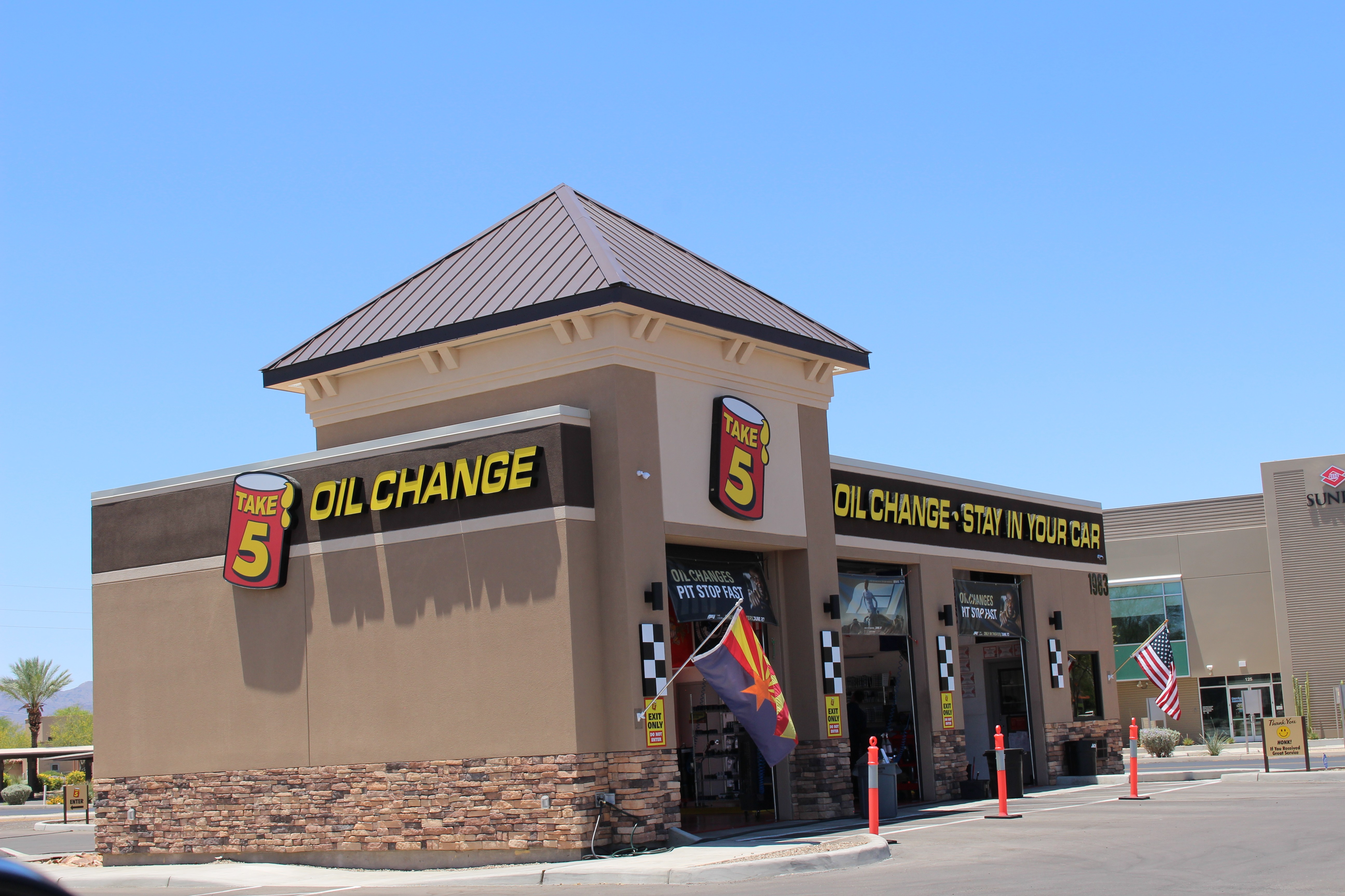 Gas station building with signs for oil change and a number 5 logo, flags, and a clear blue sky.