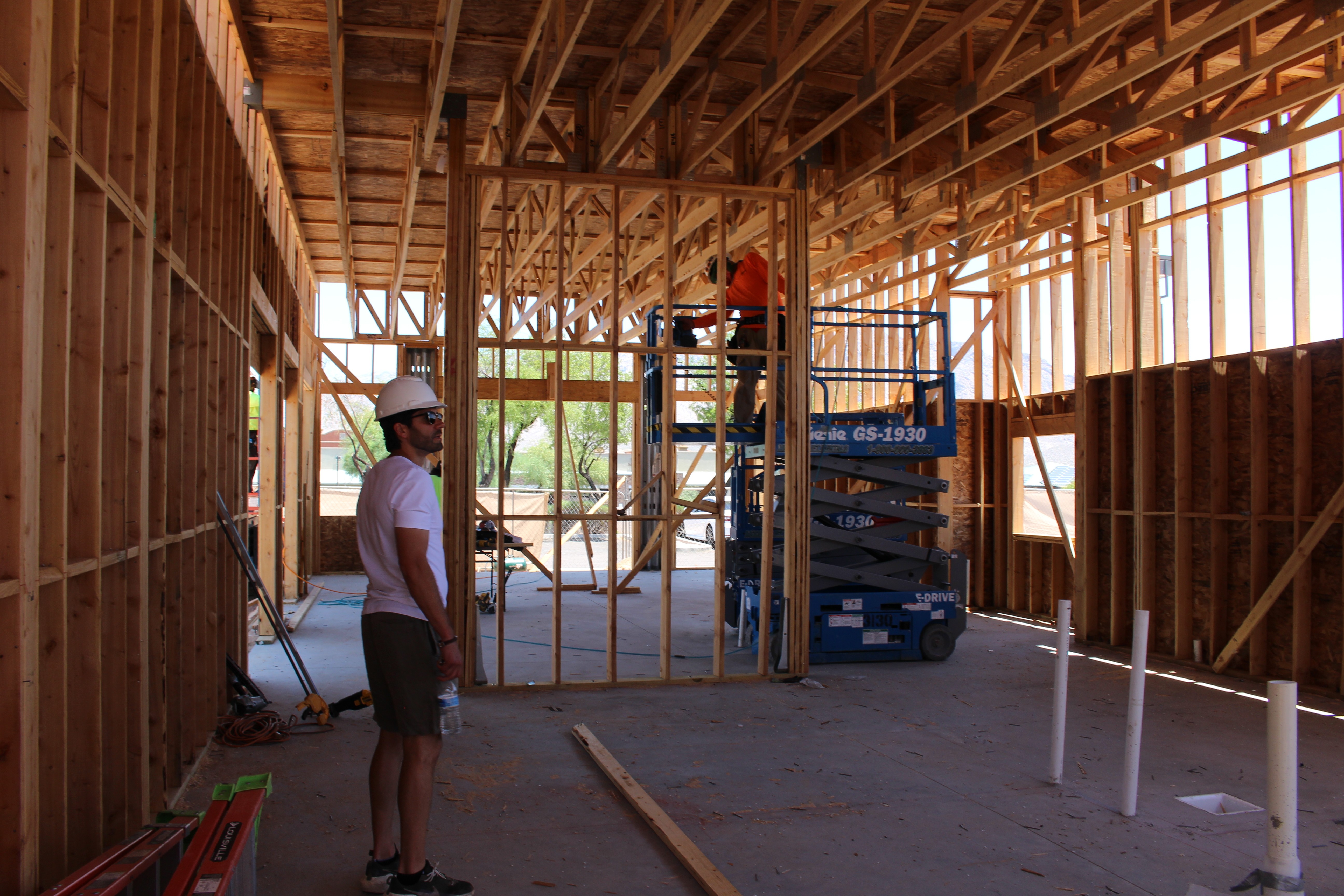 Construction site with wooden framing and a worker wearing a helmet inside a partially built structure.