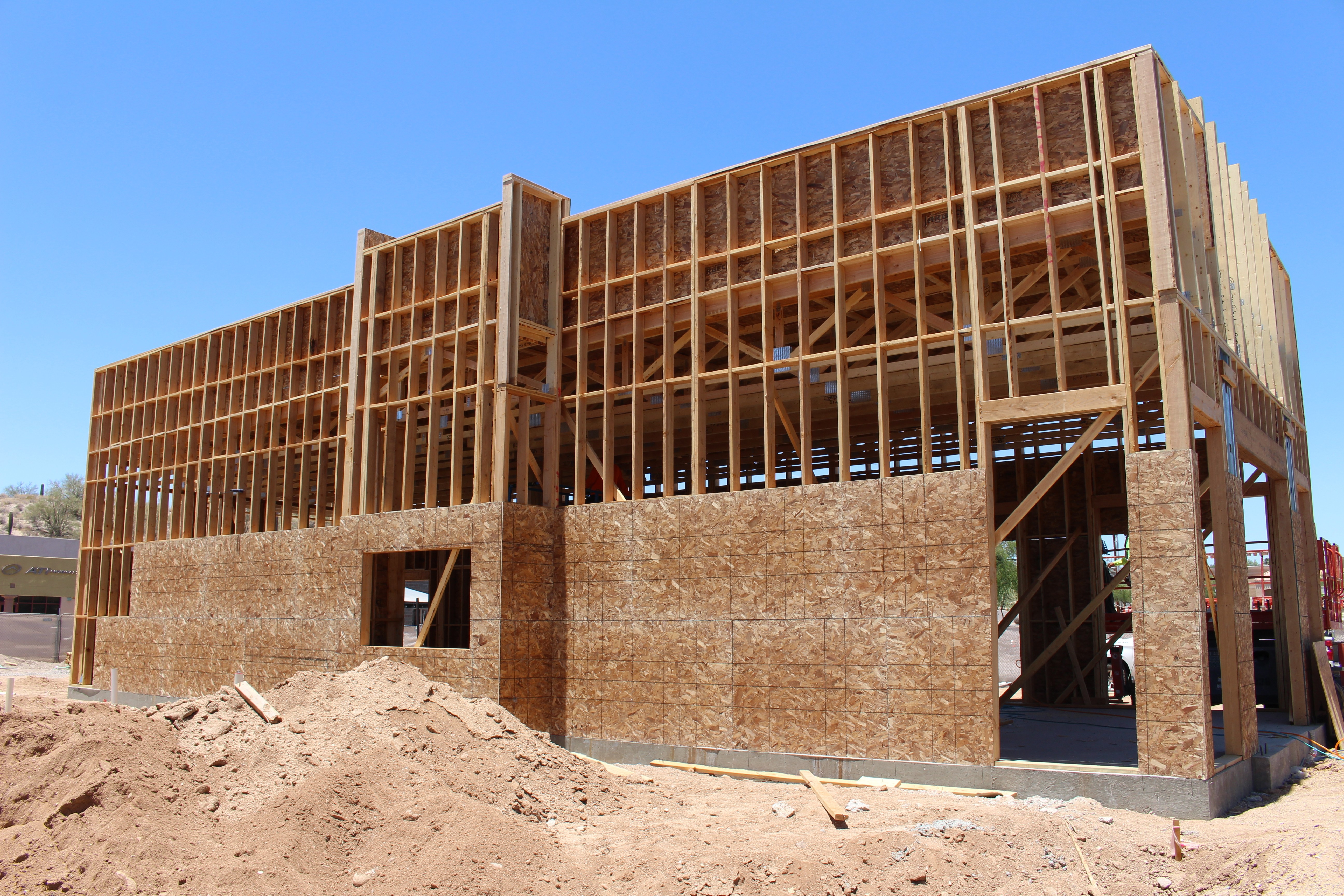Wooden building under construction with exposed framework and brick walls, set against a clear blue sky.