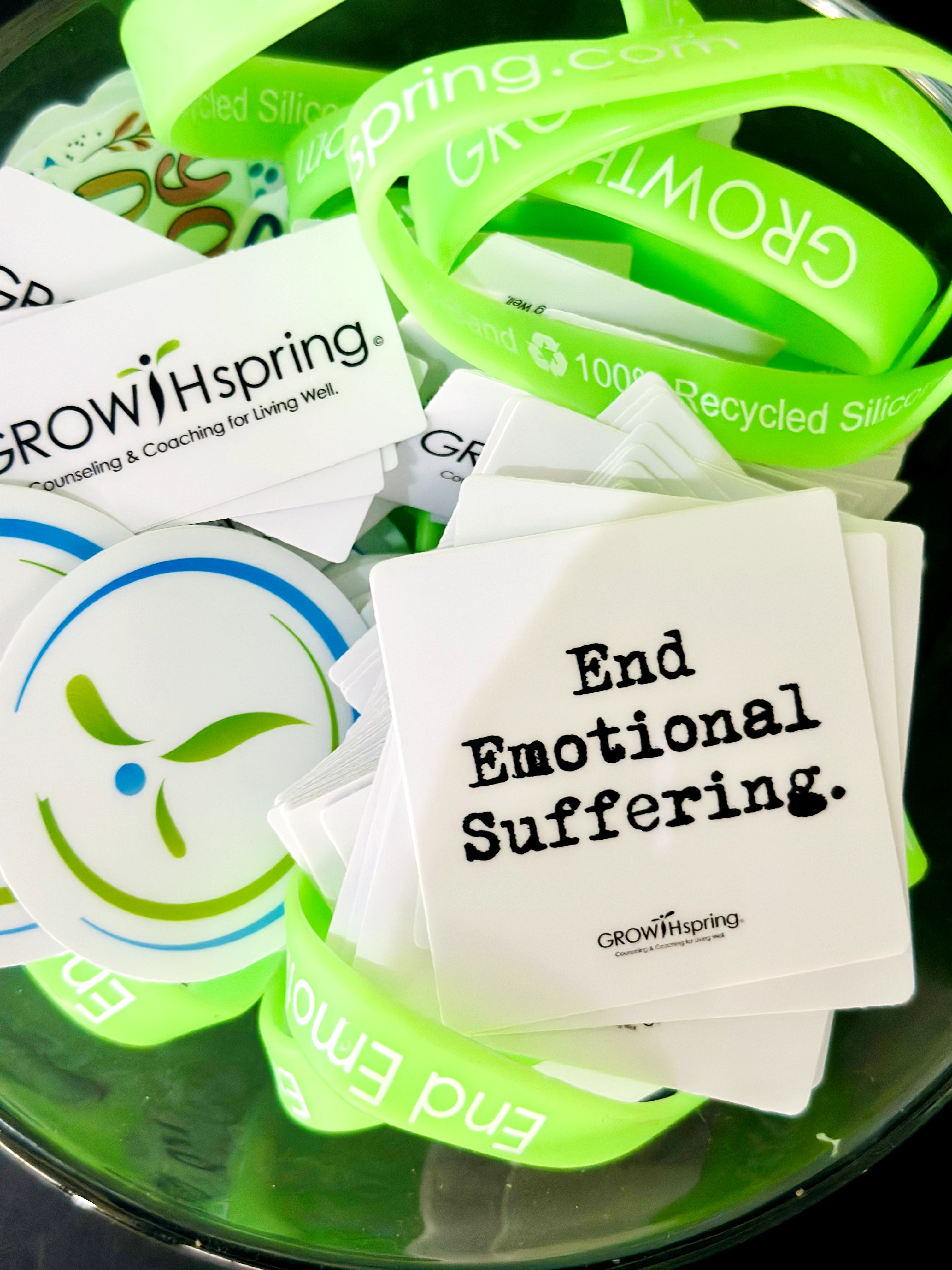 Green and white silicone wristbands, some with text, and a card with the message 'End Emotional Suffering.'