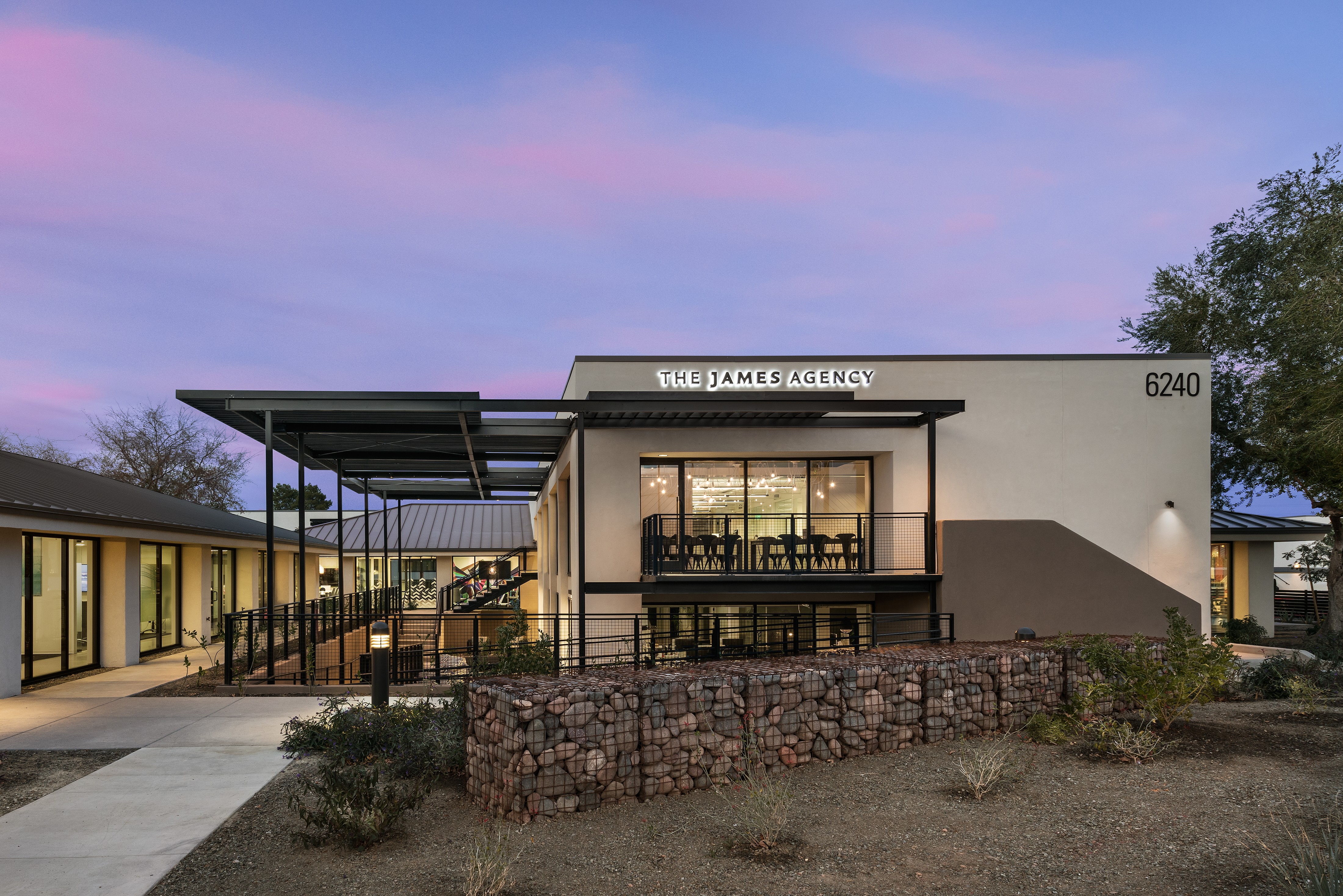 Modern building with large glass windows and a sign reading 'The James Agency' at sunset.