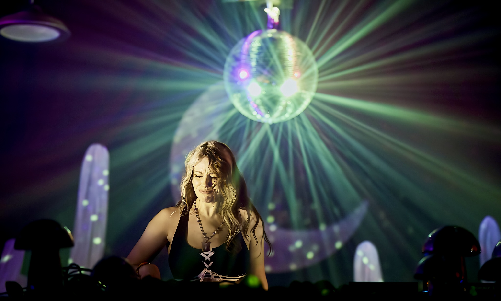 Woman with long hair in a dark setting, illuminated by a large disco ball and colorful light rays, with abstract shapes in background.