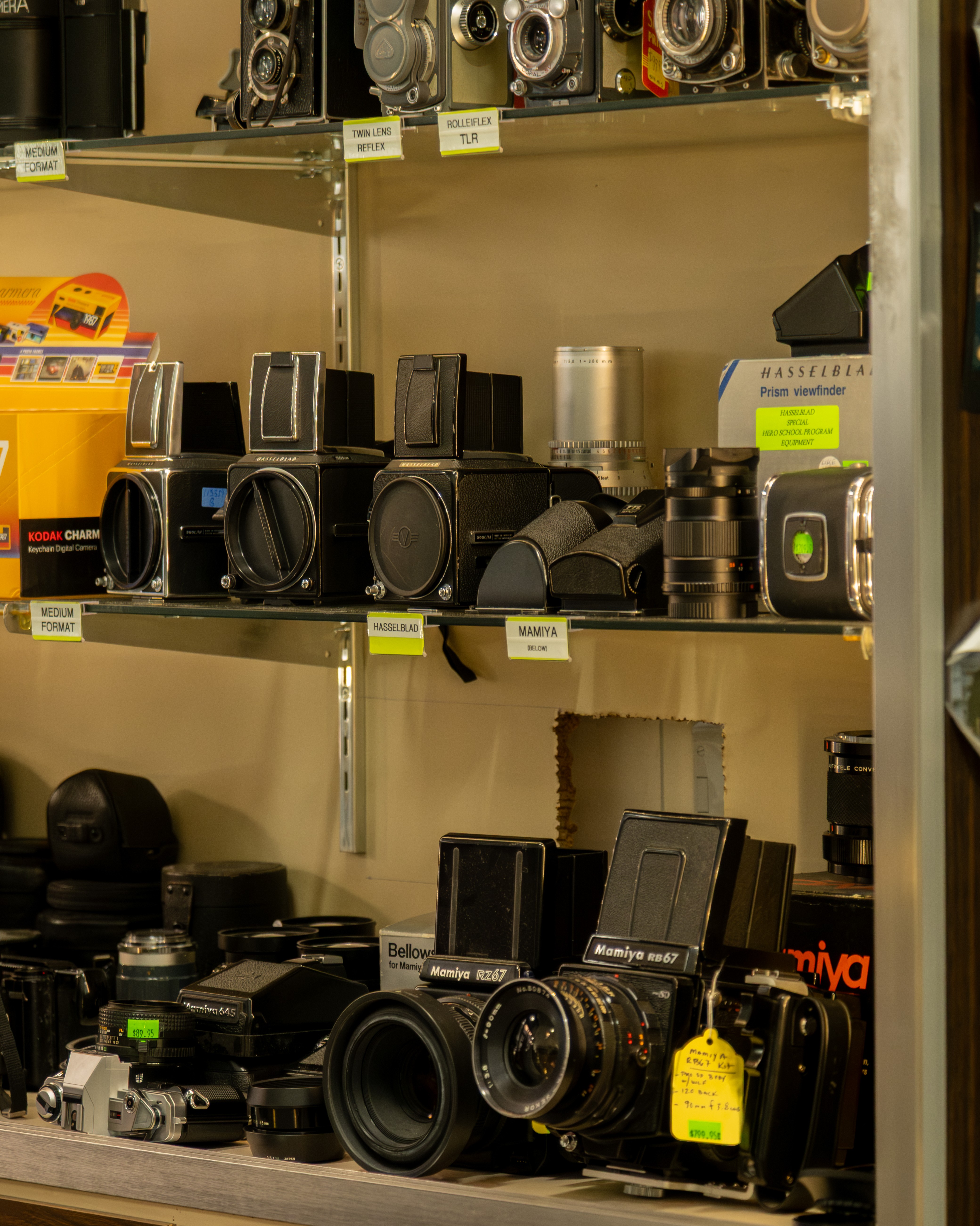 Shelves display various cameras and audio equipment in a store, with price tags visible on some items.