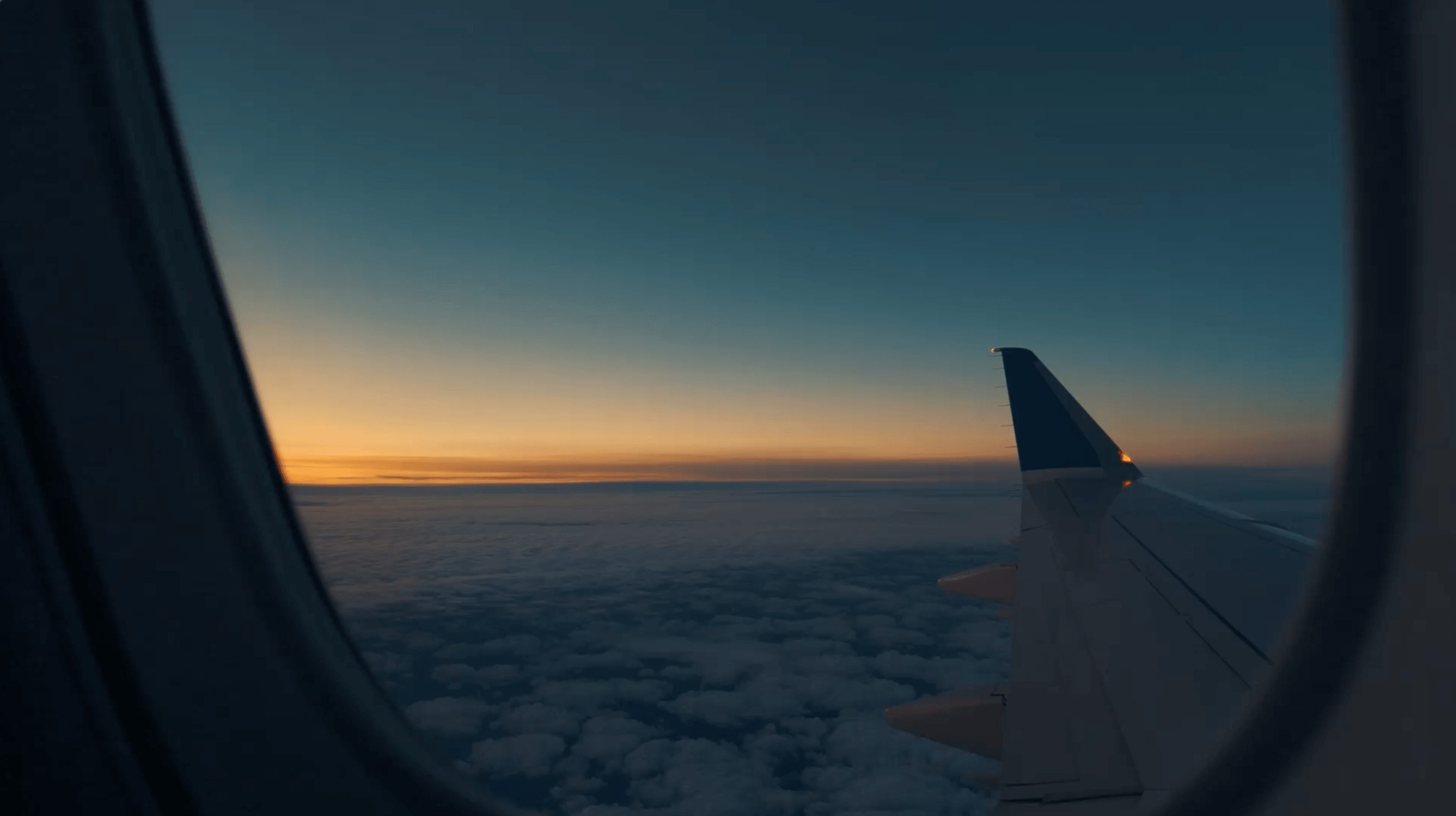 View through airplane window showing wing and sunset sky with clouds below.