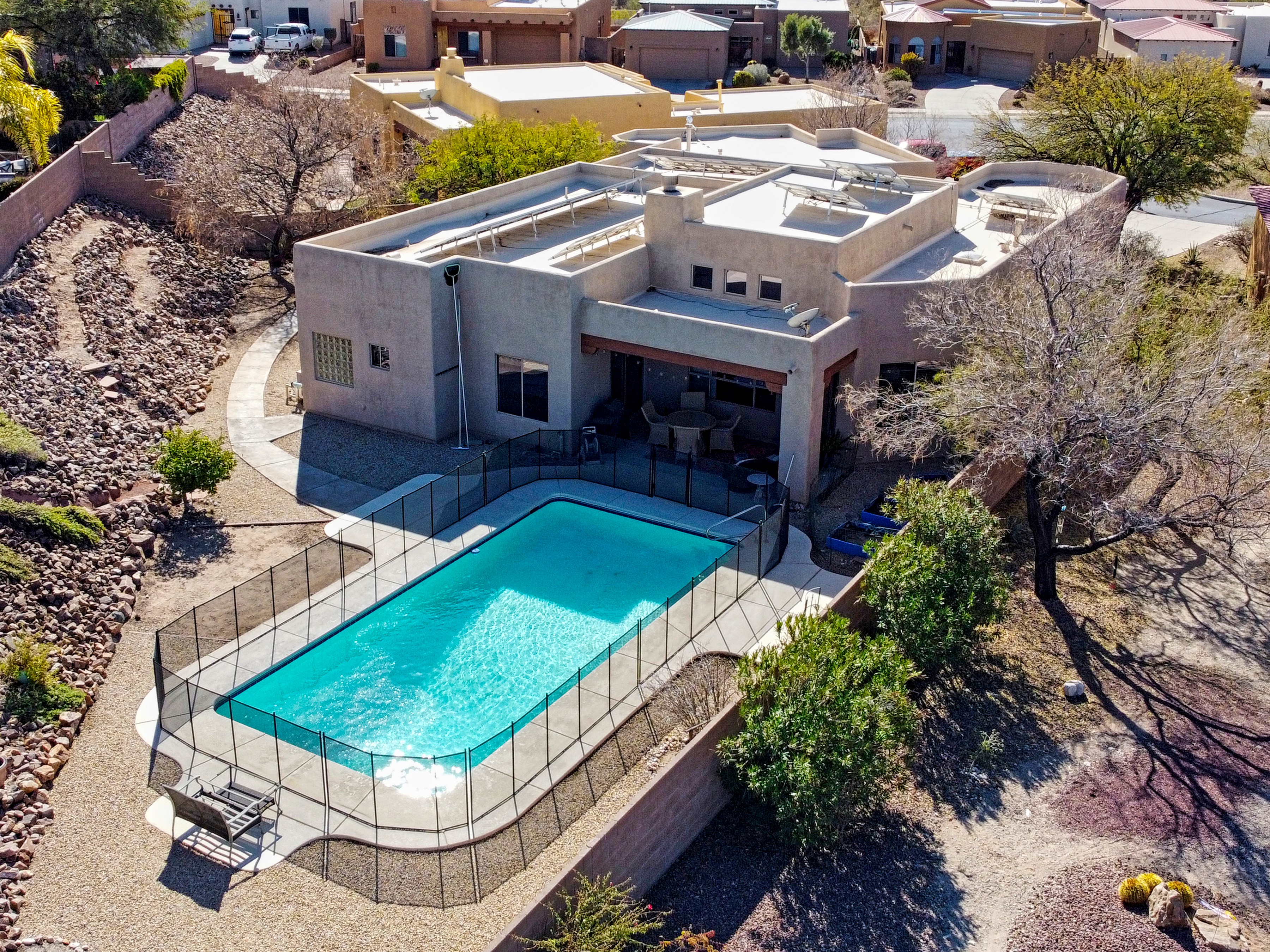Modern house with a backyard swimming pool surrounded by a fence, trees, and neighboring houses in the background.