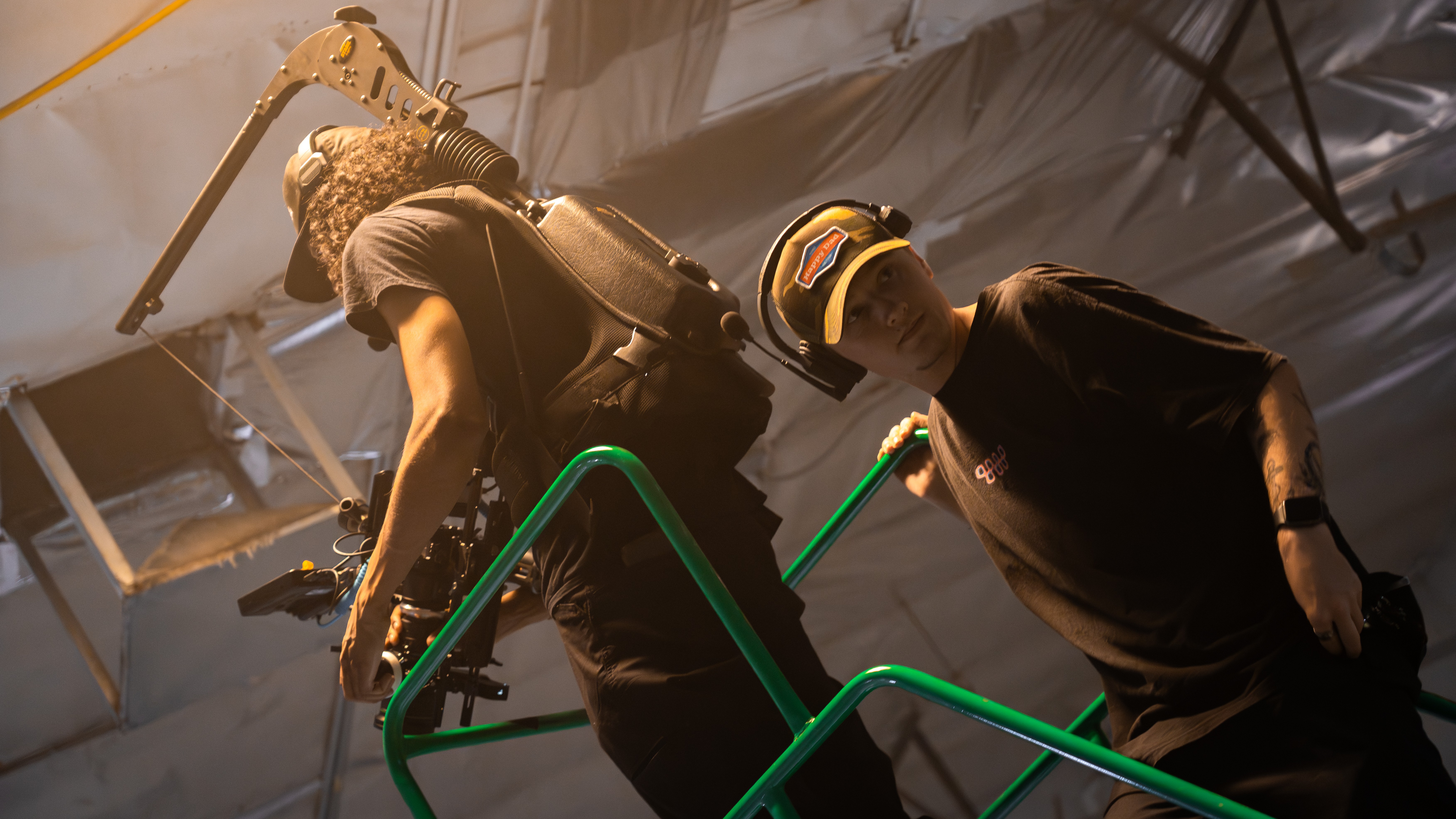 Two people, one with a helmet, stand on a green platform inside a large industrial or event space.