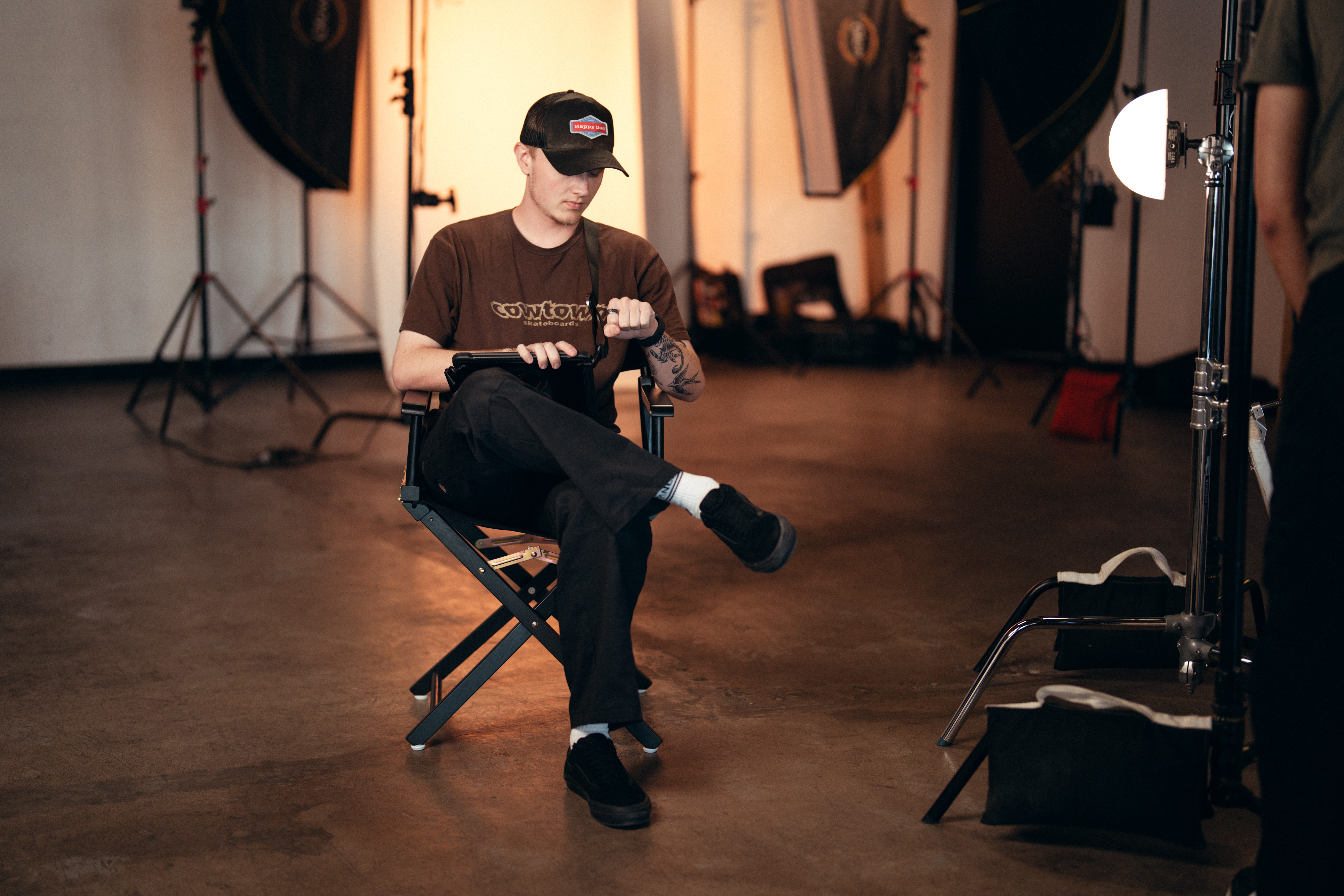 Person sitting on a chair in a studio, holding a phone, with photography equipment in the background.