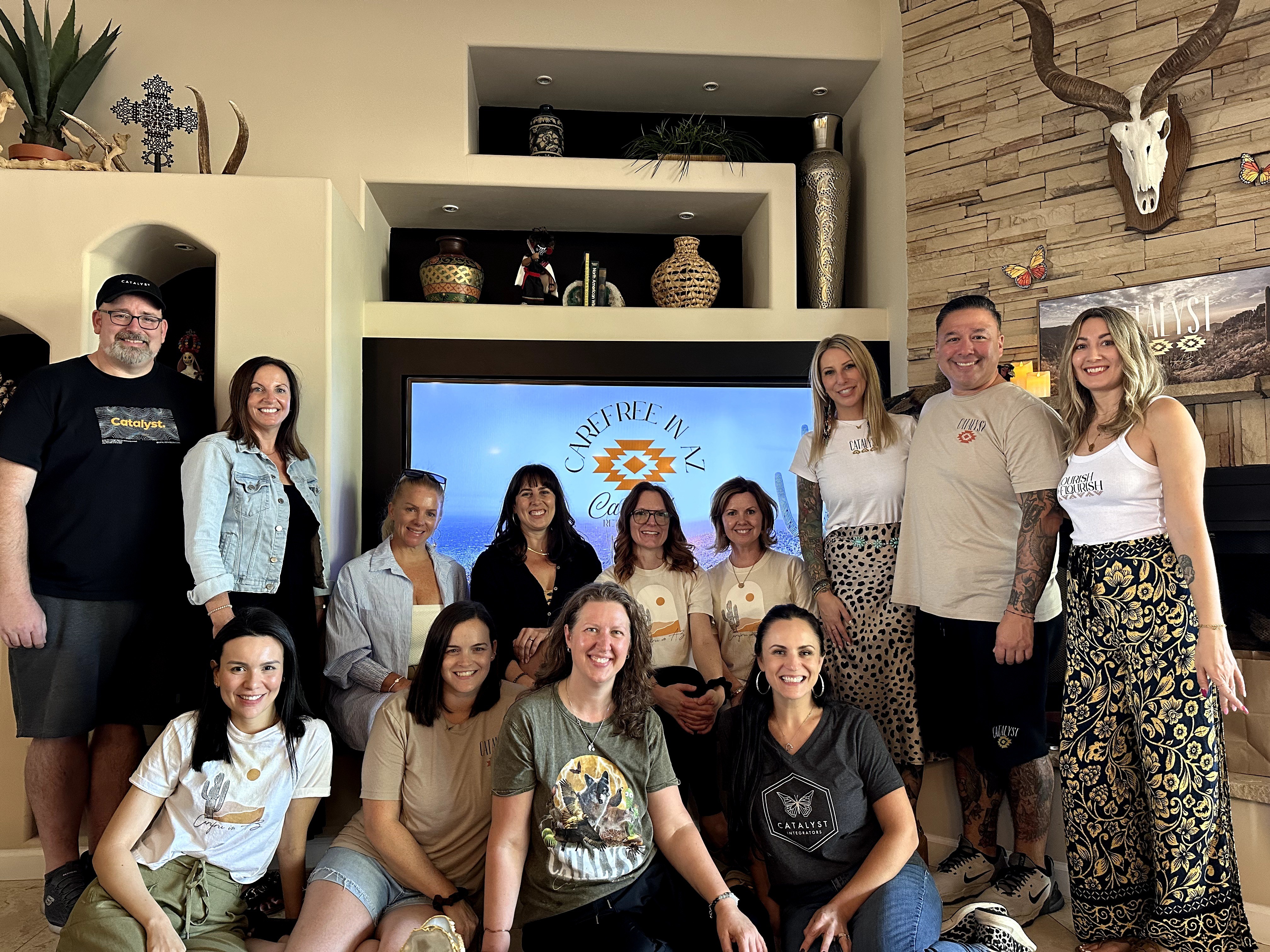 Group of eleven people posing indoors with a large screen and decorative shelves behind them.