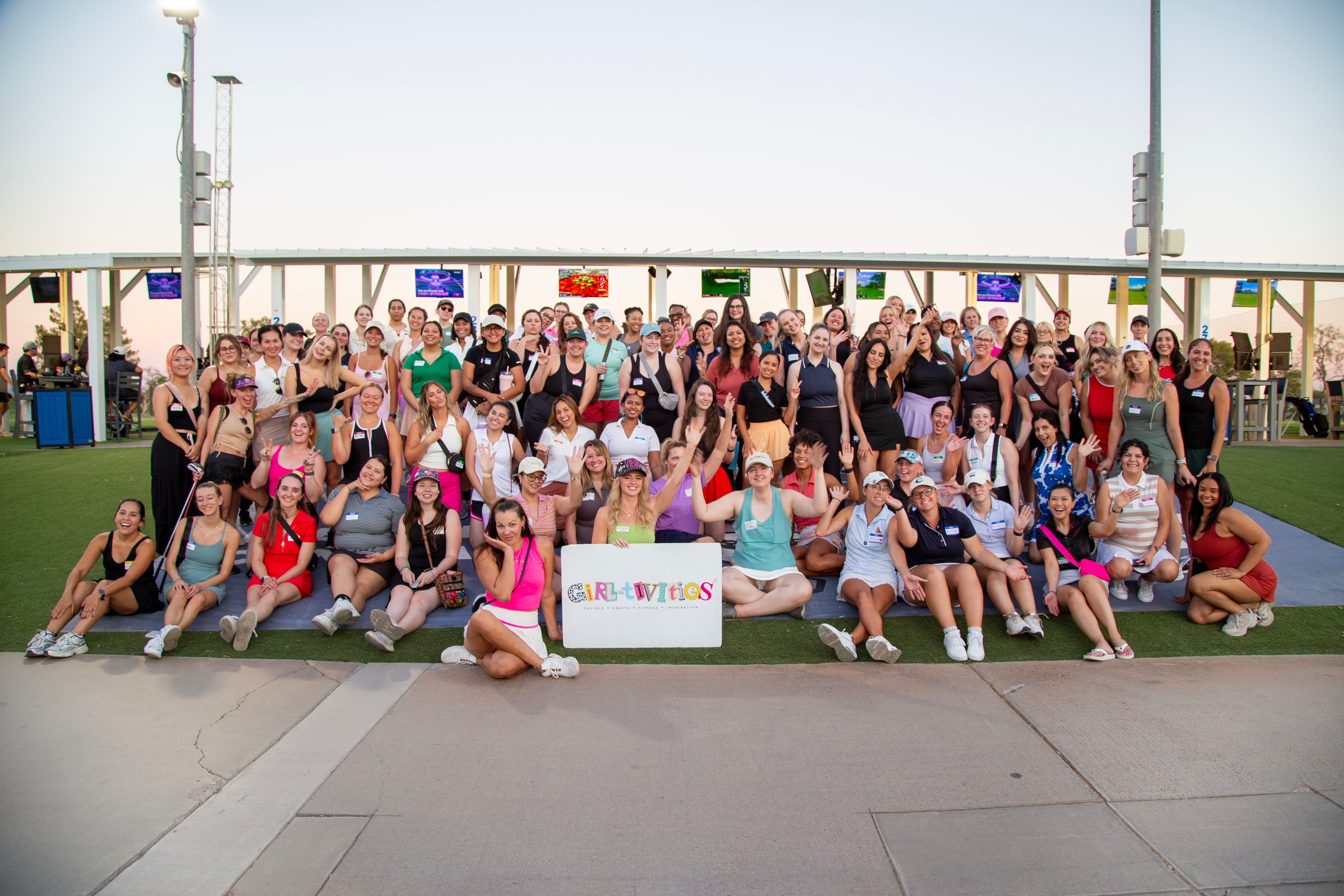 Group of people outdoors holding a sign, posing for a photo on a green surface with a railing and sky in background.