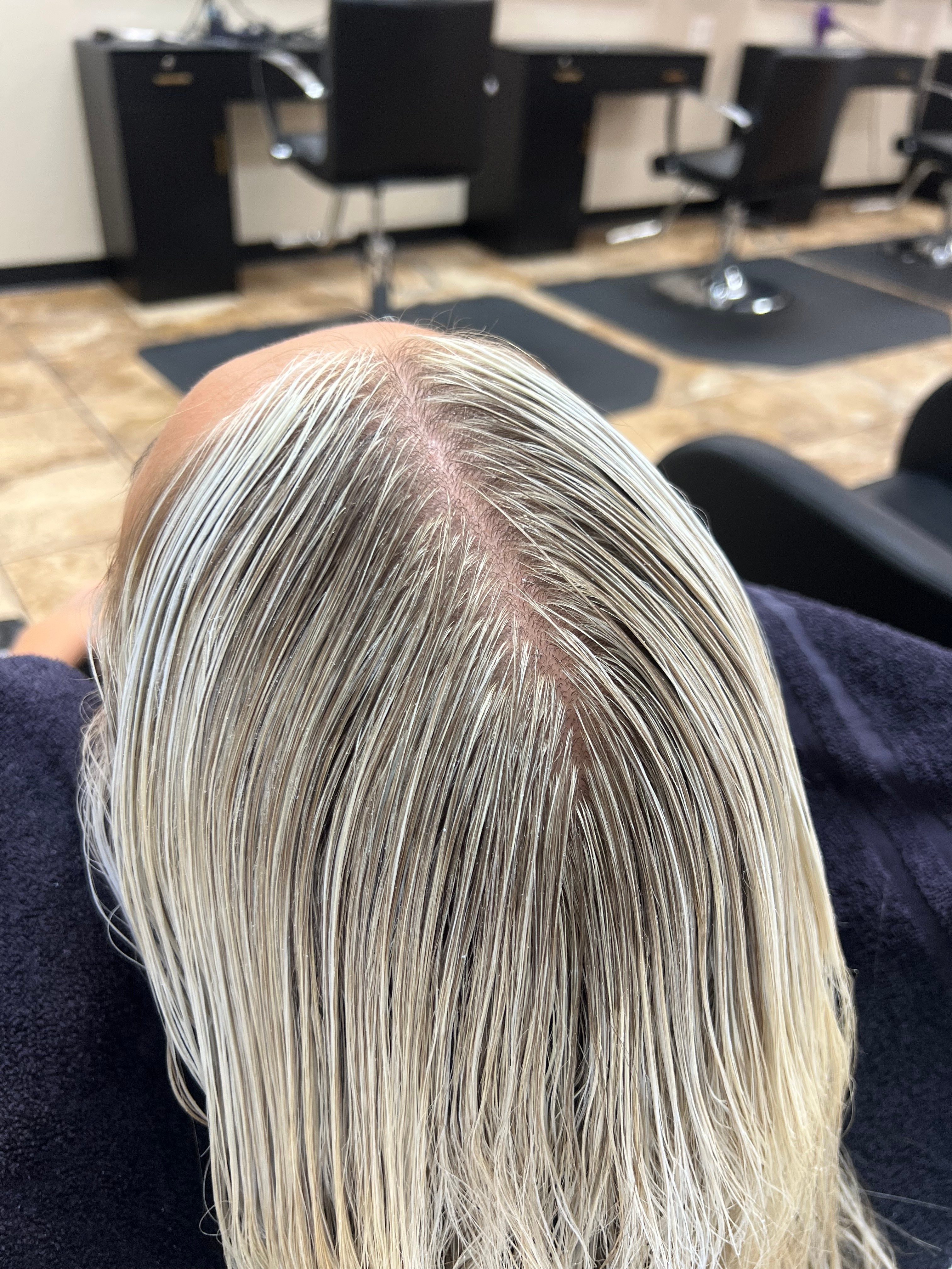 Top view of a person's straight, platinum blonde hair with a visible scalp, lying on a dark surface.
