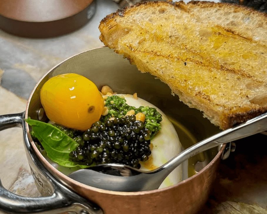 Poached egg, black caviar, and greens in a bowl with toasted bread on the side.