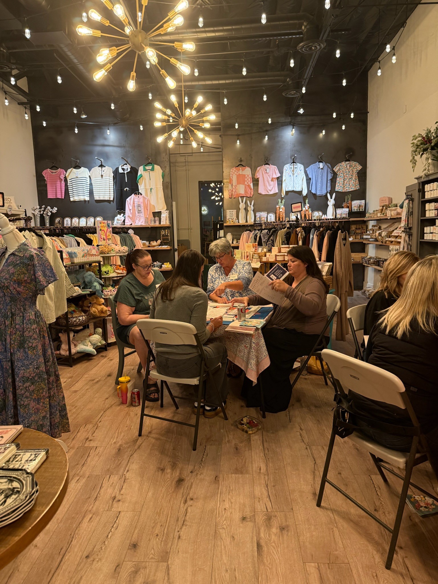 People sit around a table in a clothing store, with racks of clothes and shelves in the background.