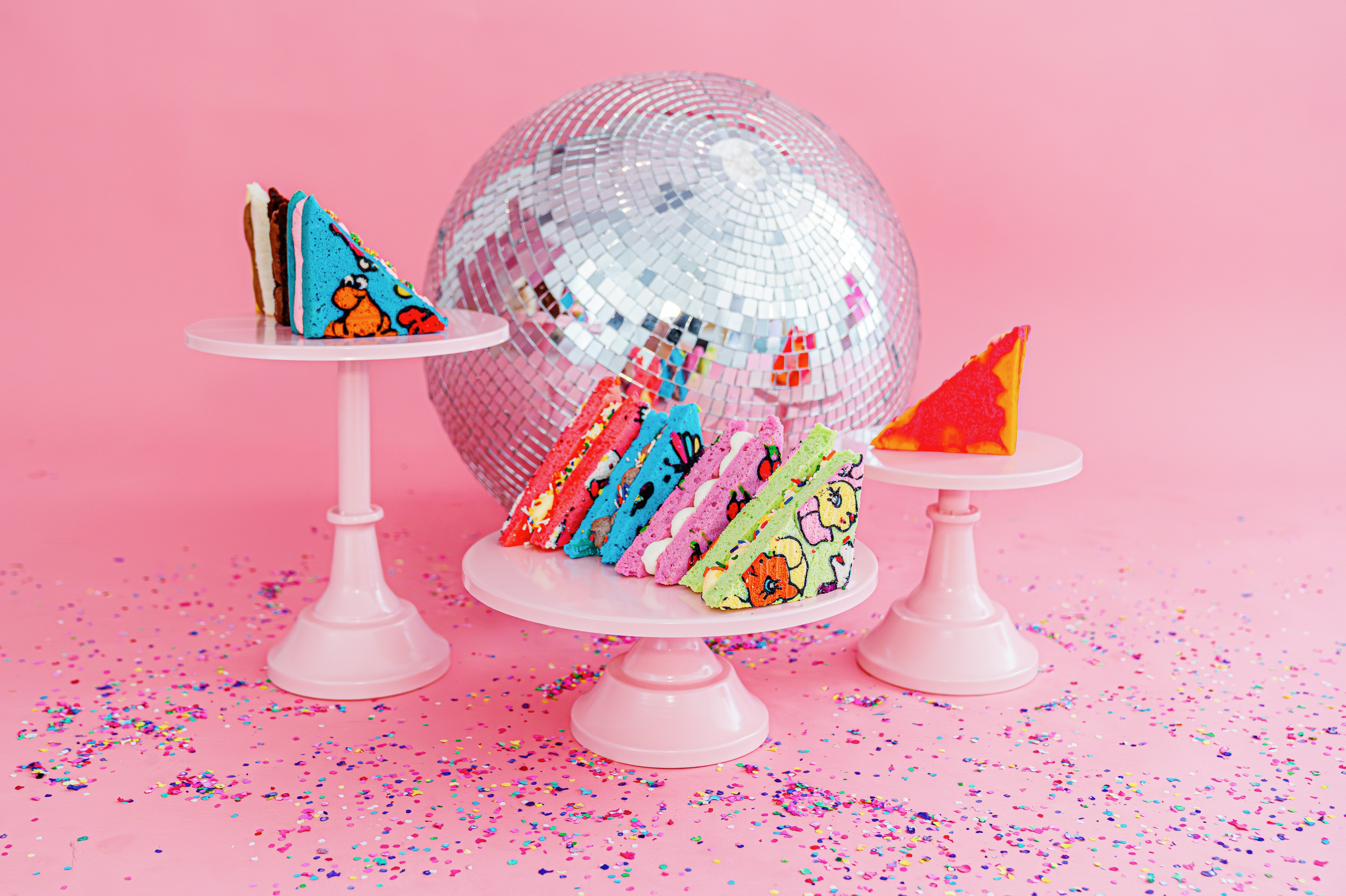 Colorful cake slices on pink cake stands with a disco ball on a pink background, surrounded by confetti.