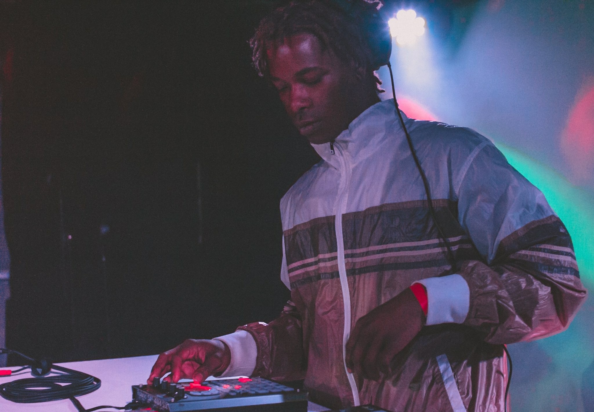 Person with headphones operating electronic music equipment in a dimly lit setting.
