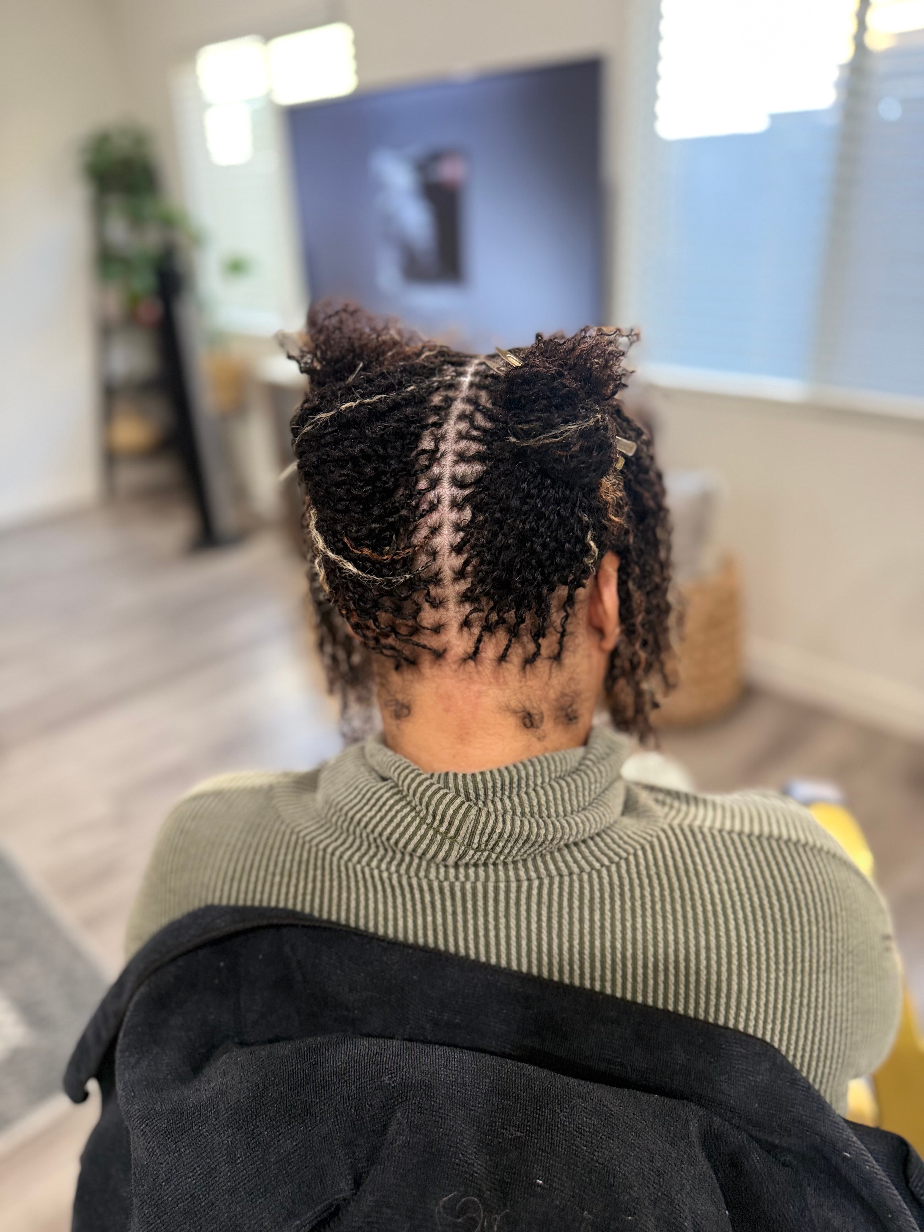Back view of person with short curly hair styled in two sections, sitting in a room with a TV and window.