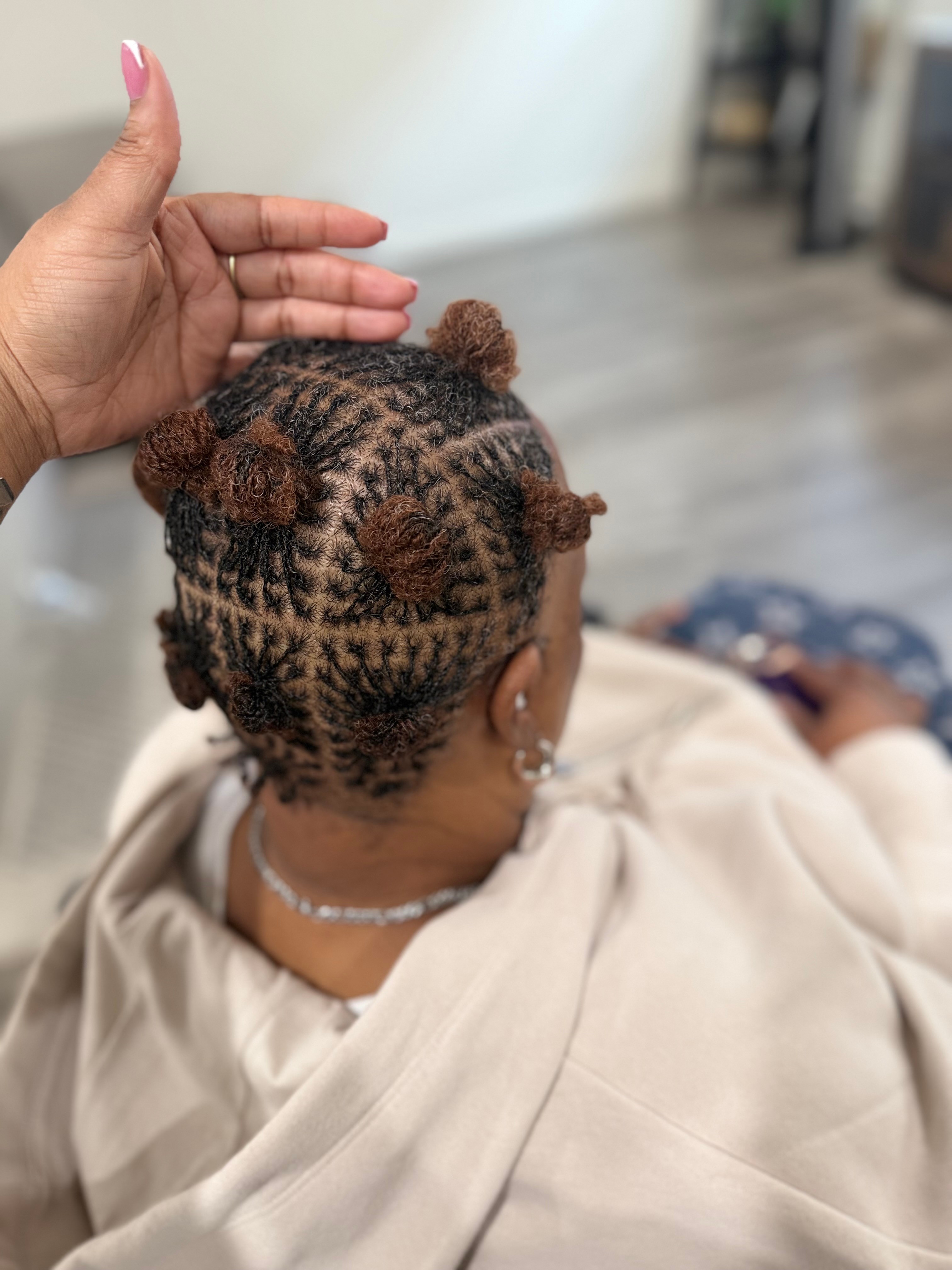 Child with braided hair styled into small buns, sitting on a beige blanket, with a hand gently touching their head.