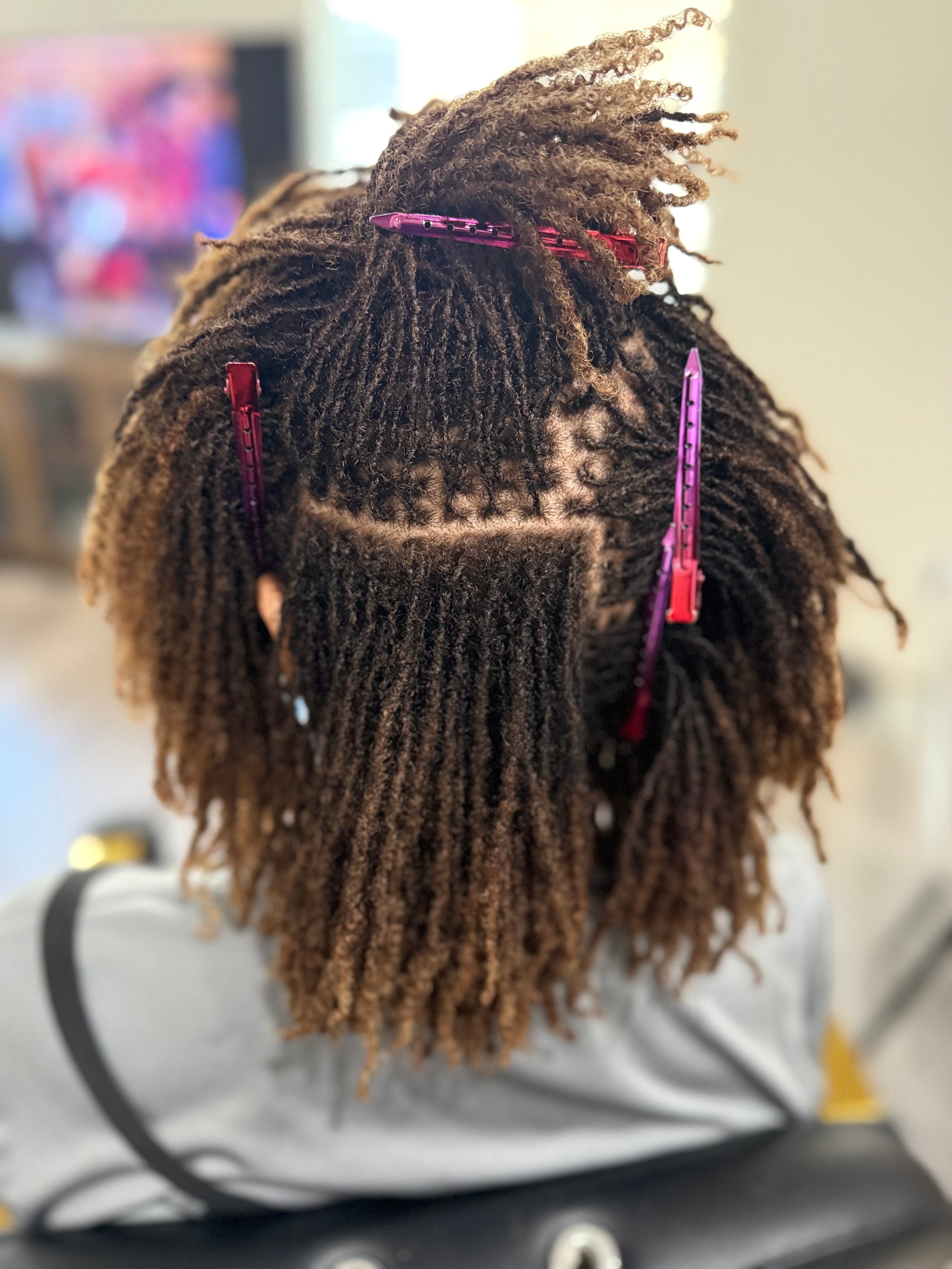 Back of person's head with styled dreadlocks and hair clips, in a salon setting