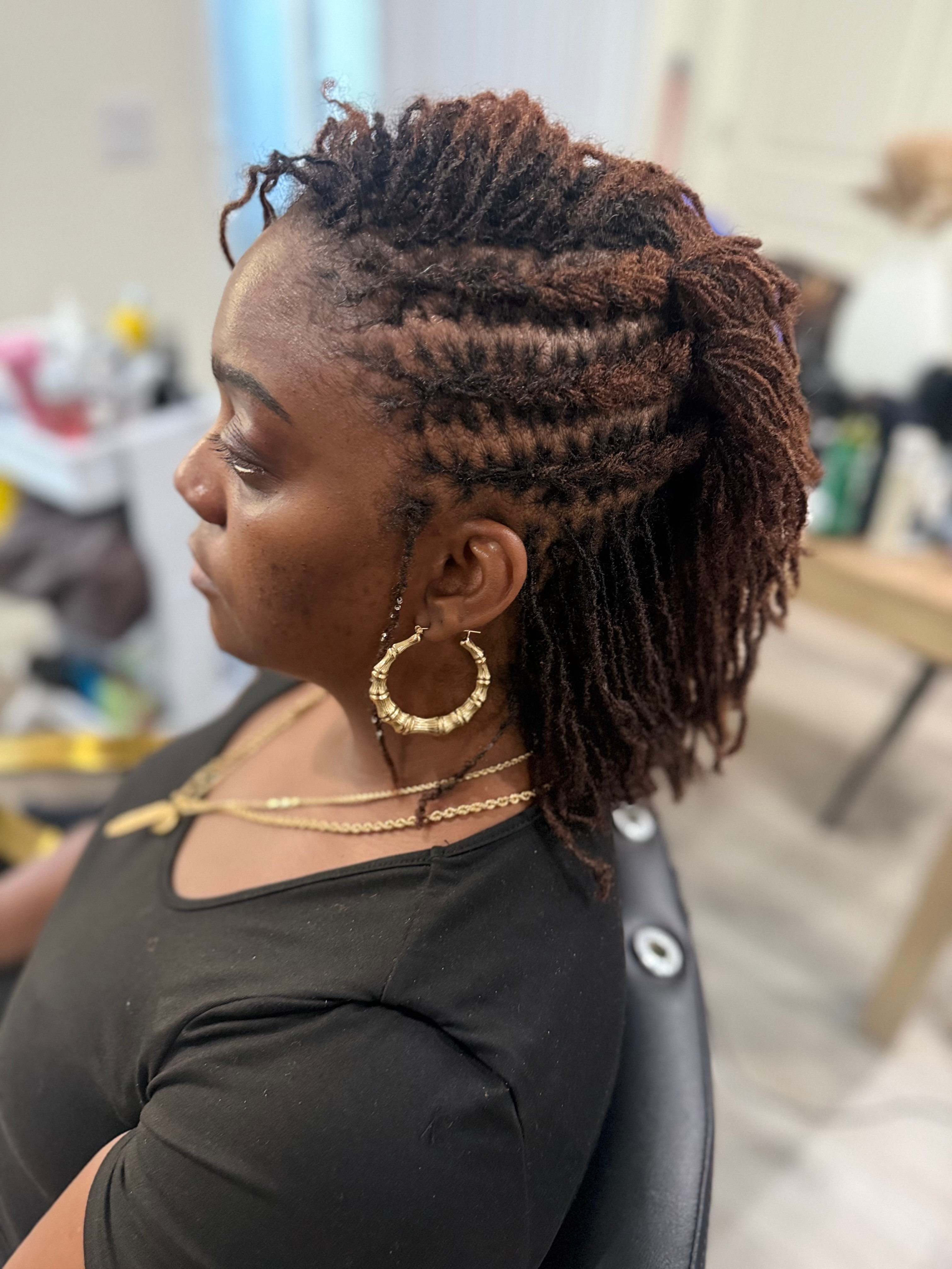 Side view of a woman with styled dreadlocks, wearing large hoop earrings and a black top, in a salon setting.