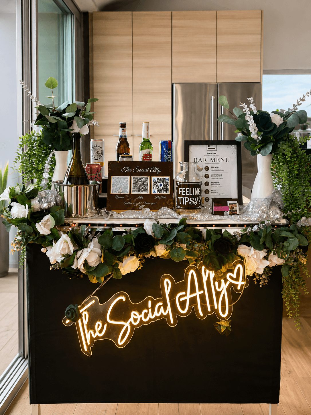 Bar setup with flowers, drinks, and a neon sign reading 'The Social Ally' in a modern kitchen.
