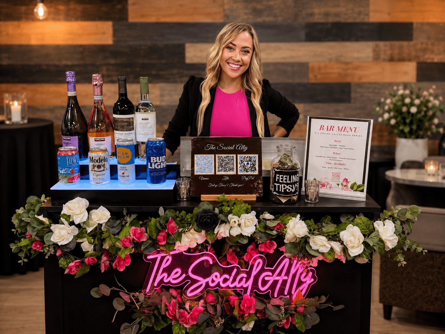Smiling woman behind a bar with bottles, flowers, and a menu, decorated with pink and white flowers, and a neon sign reading 