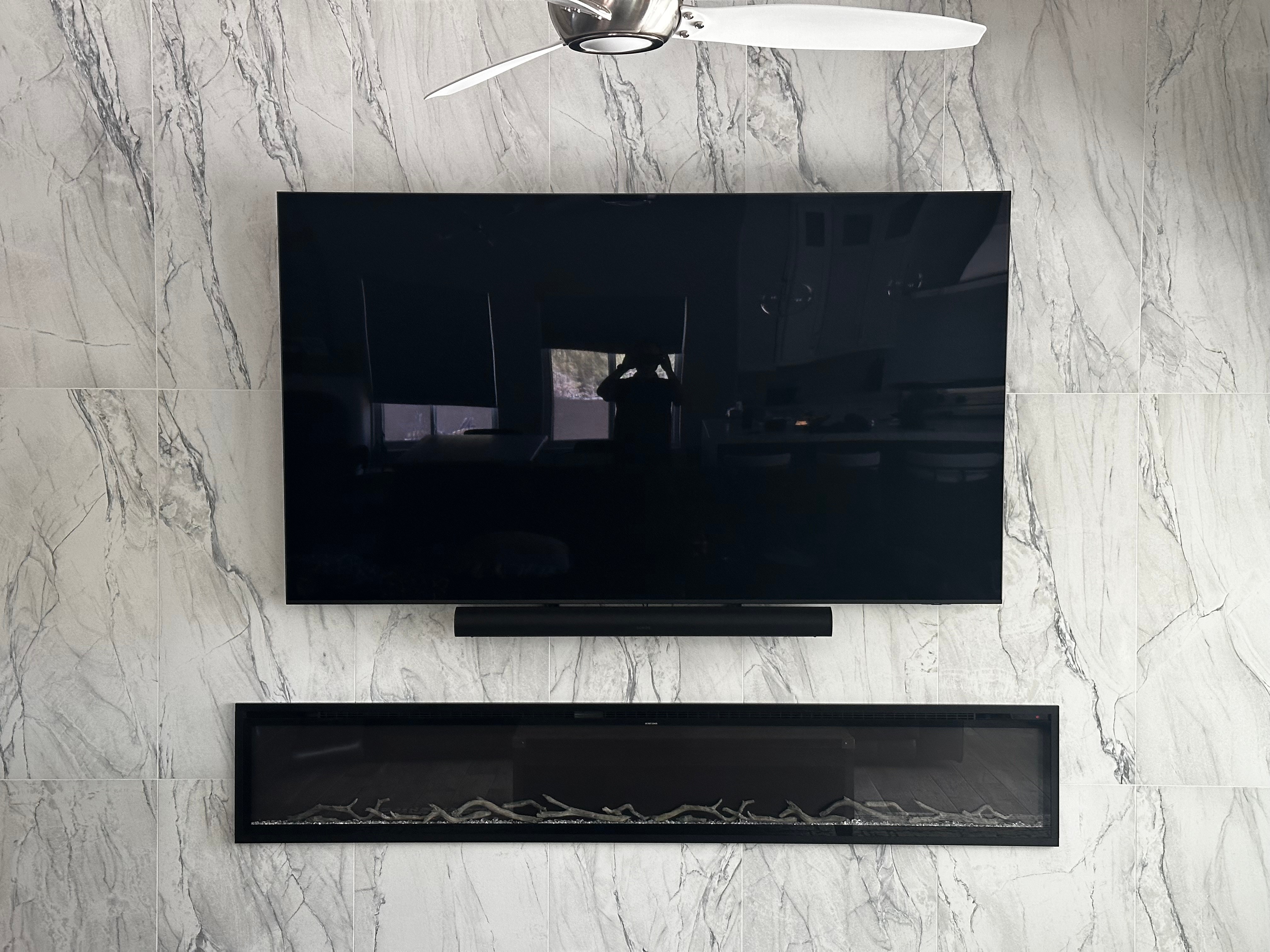 Flat-screen TV mounted on a marble wall with a soundbar below and a ceiling fan above