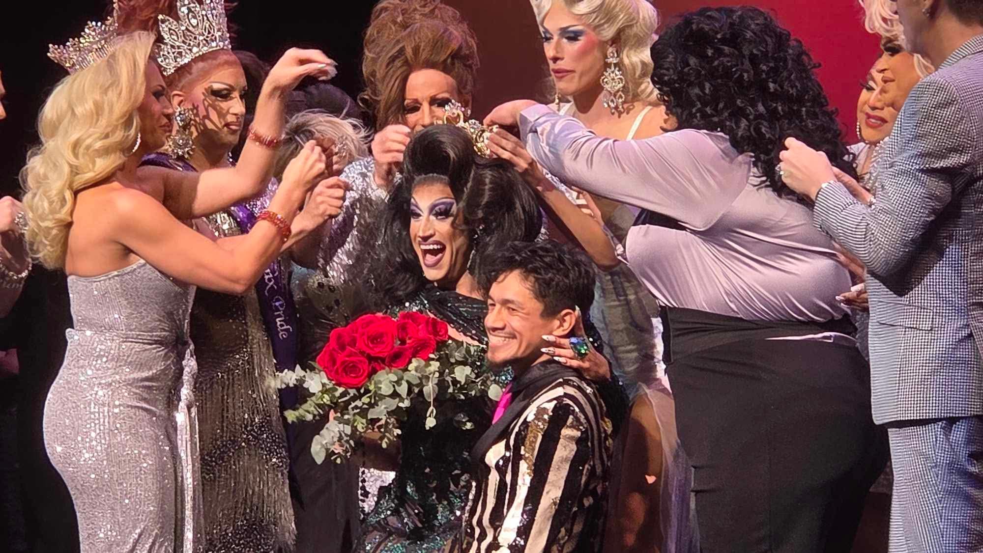 Group of people celebrating with a person holding a bouquet of red roses, on stage with colorful background.