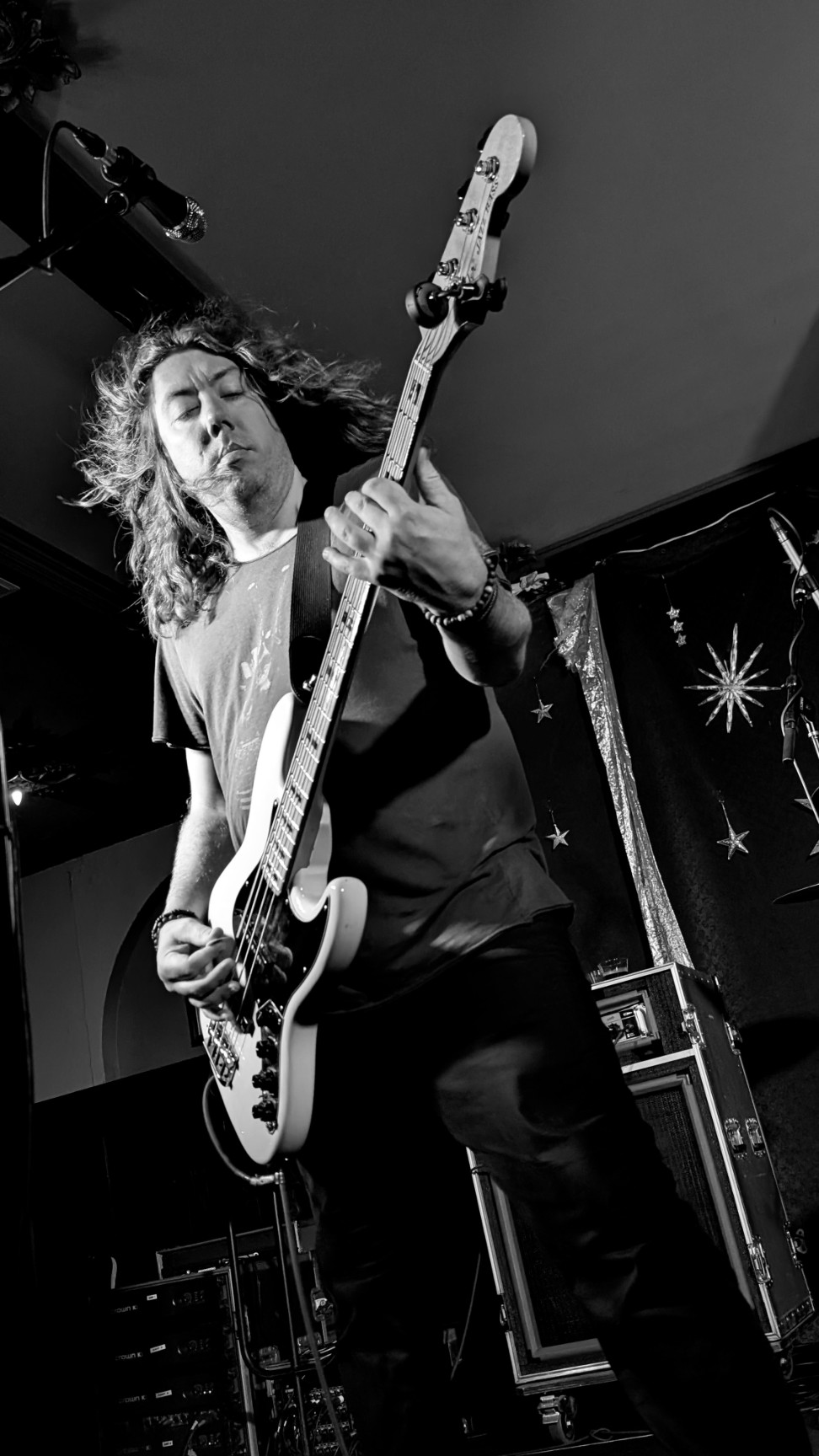 Person playing an electric guitar on stage with a starry backdrop, black and white image.
