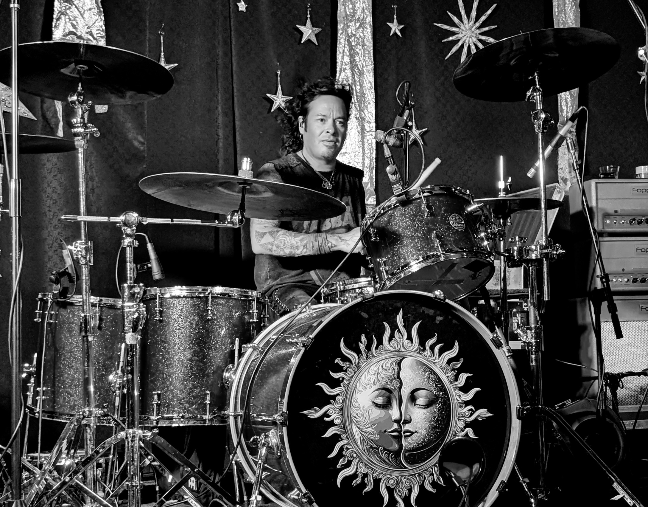 A person playing drums on stage with celestial decorations, including stars and a sun and moon motif on the drum.