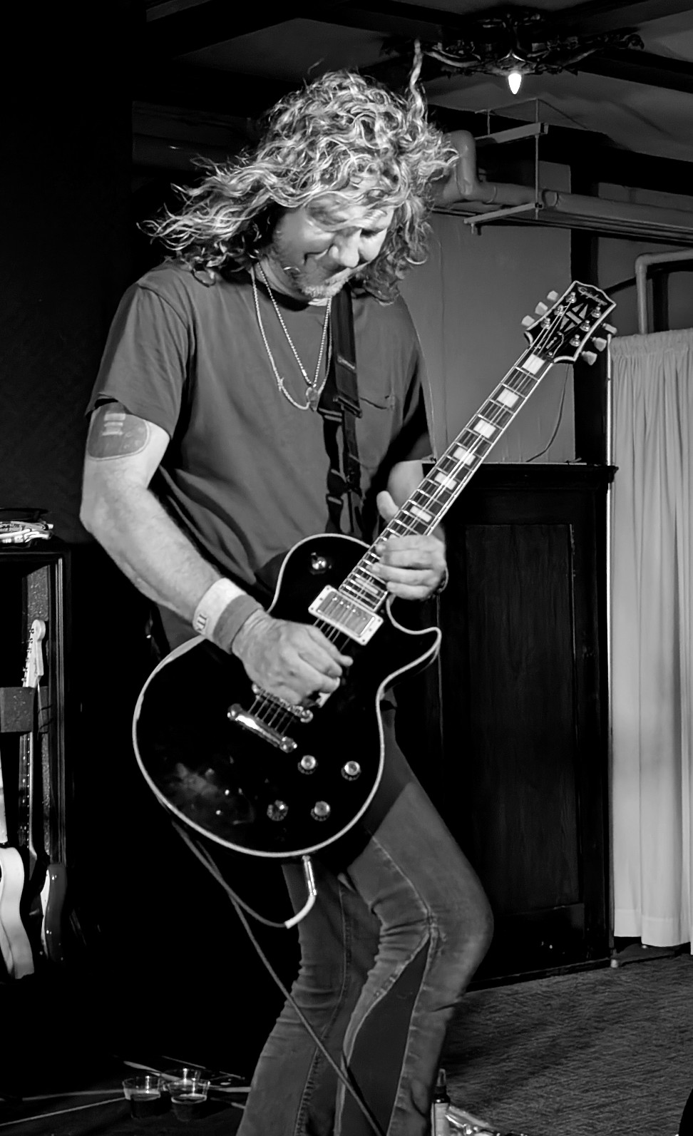 Person with curly hair playing an electric guitar on stage, black and white image.